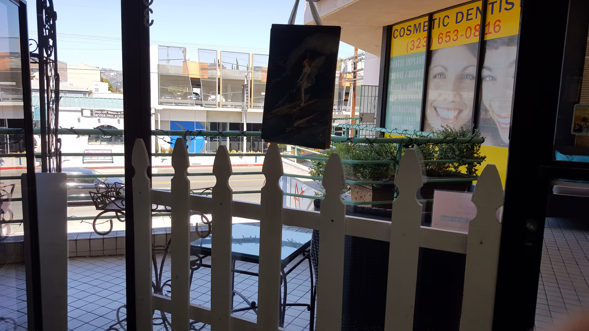 View through glass doors of an outdoor patio with a white picket fence and seating.