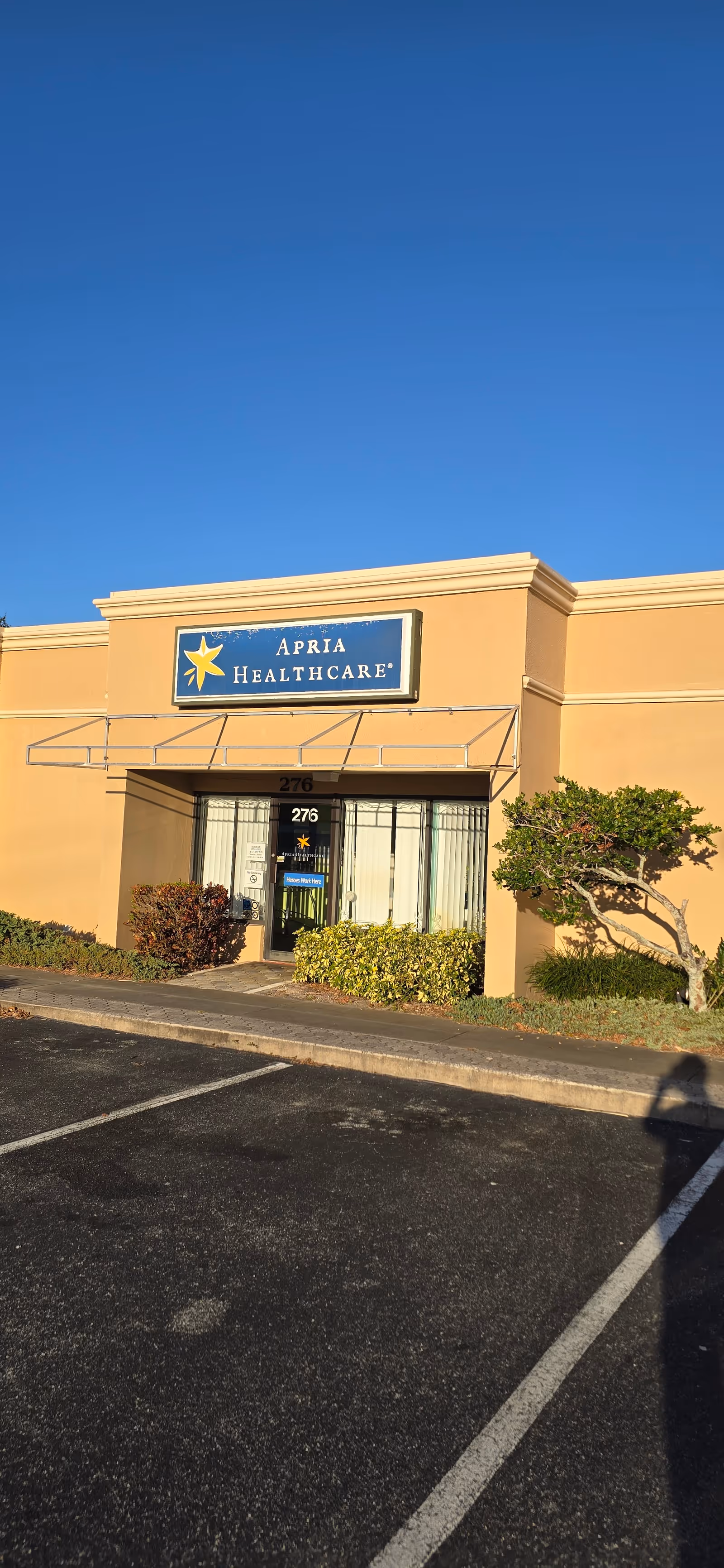 Exterior view of Apria Healthcare entrance on tan building with a parking lot.
