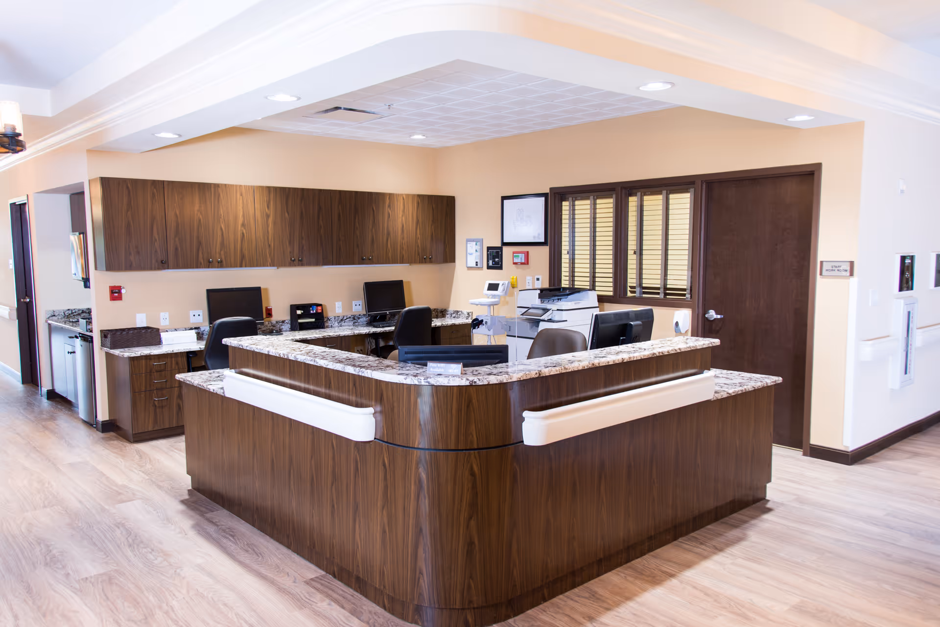 Curved wooden reception desk with granite counter in a warmly lit hospice care lobby.