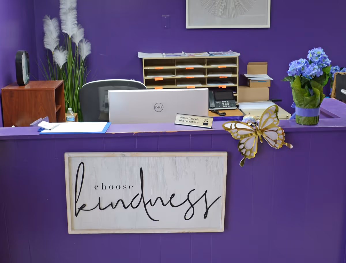 Purple front desk reception area with butterfly decor, plants, and organized mail shelves.
