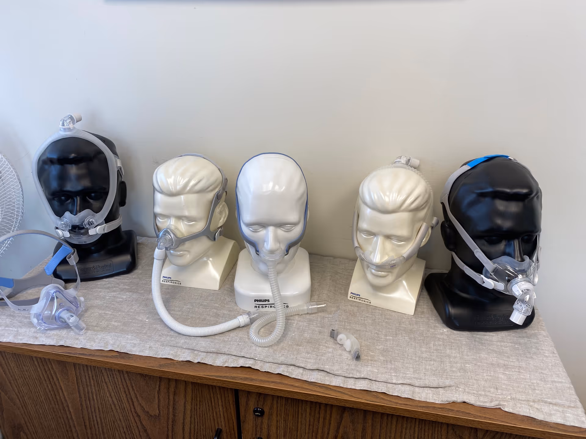 Row of CPAP masks on mannequin heads arranged on a table in a plain room.