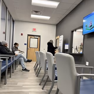 Waiting area inside a facility with chairs, a reception desk, and a wall-mounted TV.