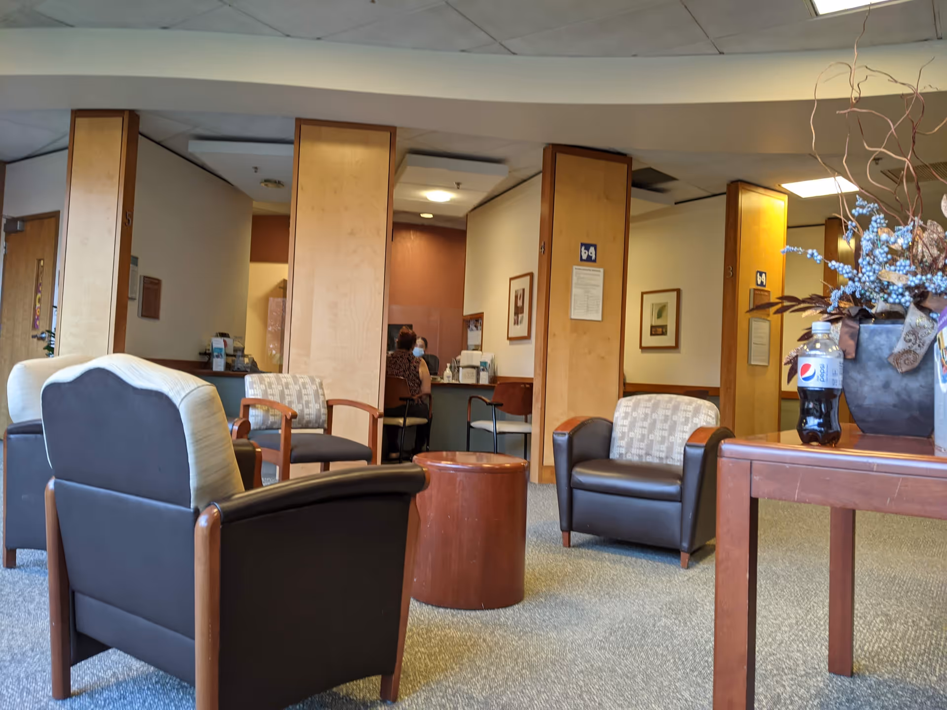 A hospital lobby lounge with brown chairs, a table, and a receptionist desk in the back.