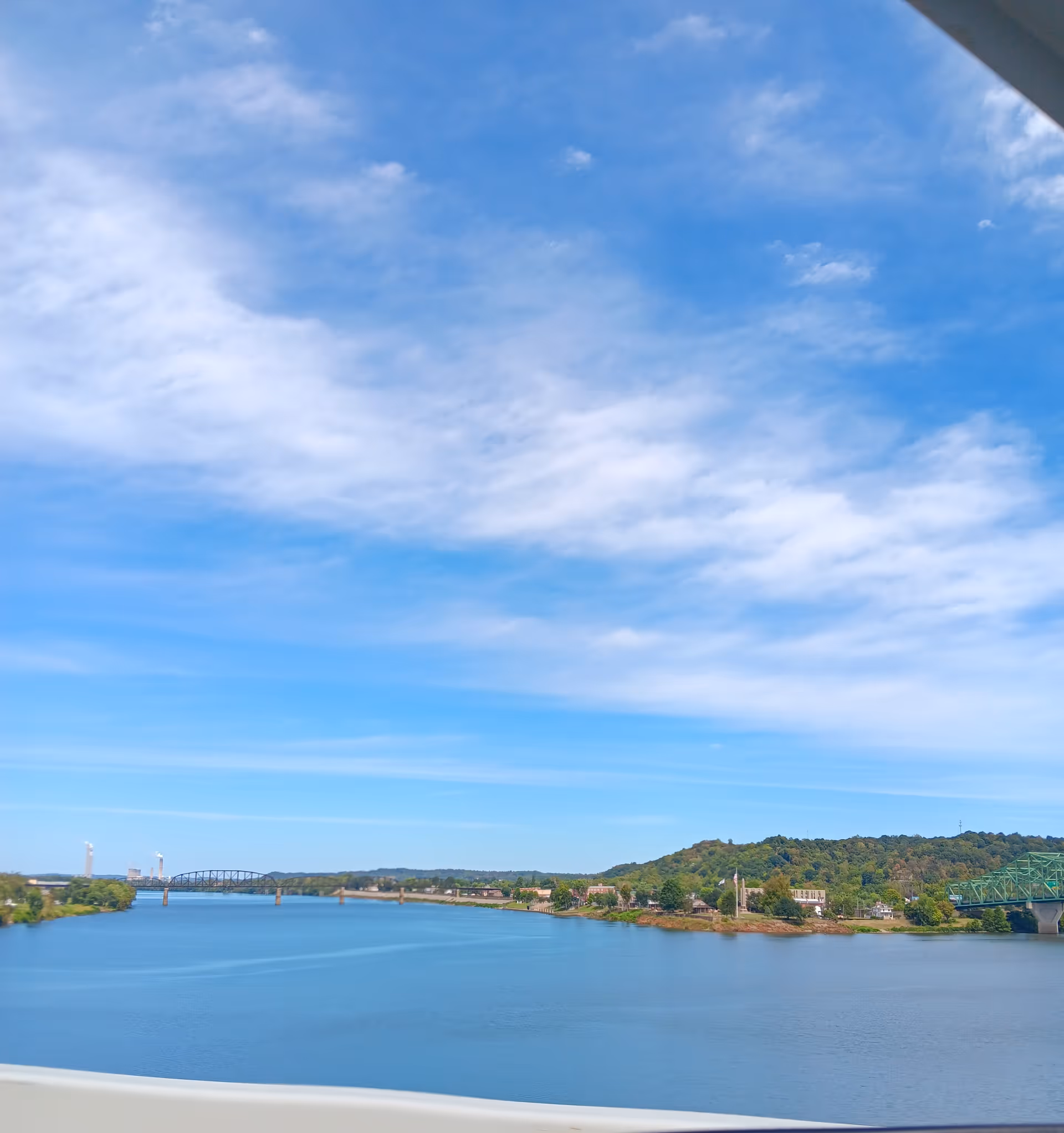 Wide river landscape with blue sky, clouds, a distant bridge, and shoreline.