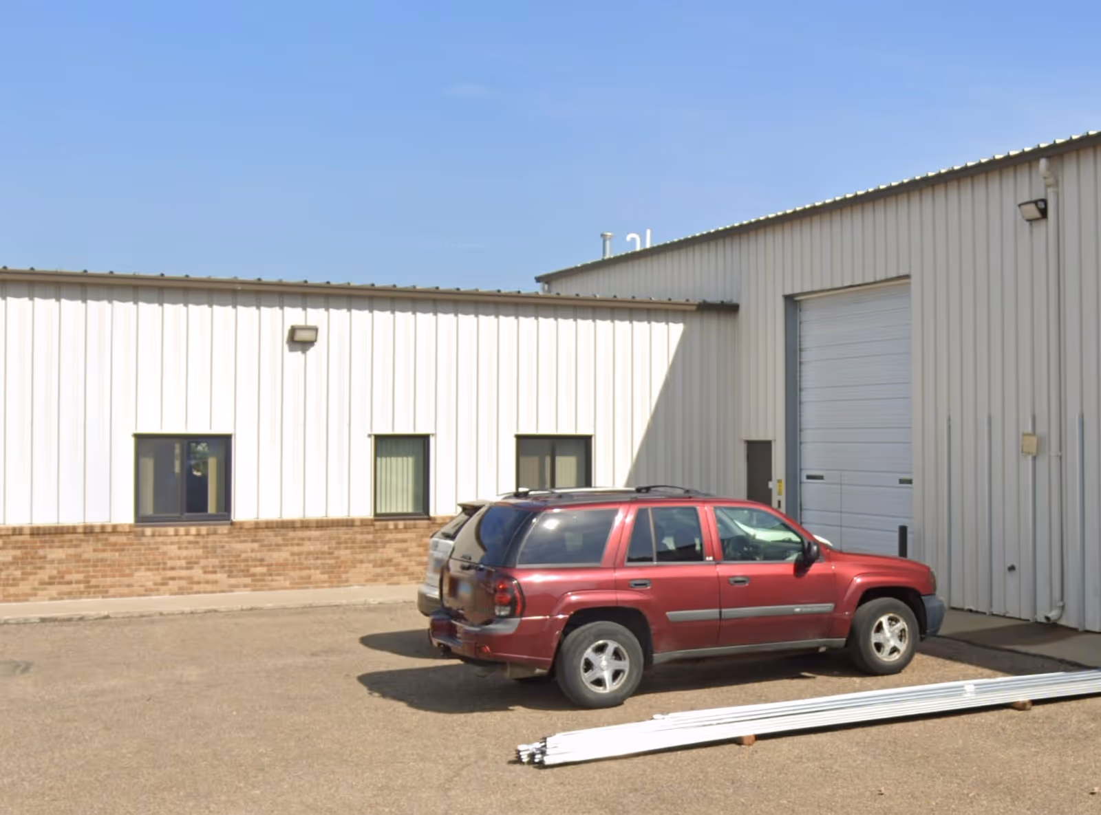 Exterior view of a white metal building with a red SUV parked in front.