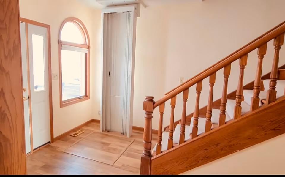 Entry hall with wooden staircase railing, front door, and a nearby elevator shaft.
