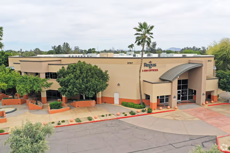 Exterior view of a beige senior care facility with curved entrance and palm trees.
