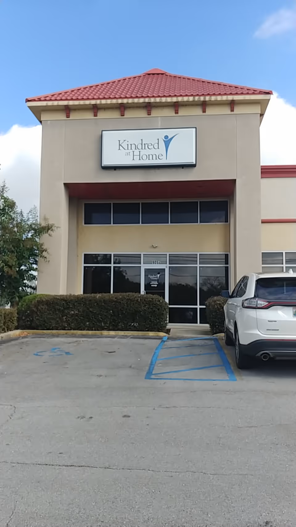 Front of a beige Kindred at Home building with a glass entry and blue handicap parking.