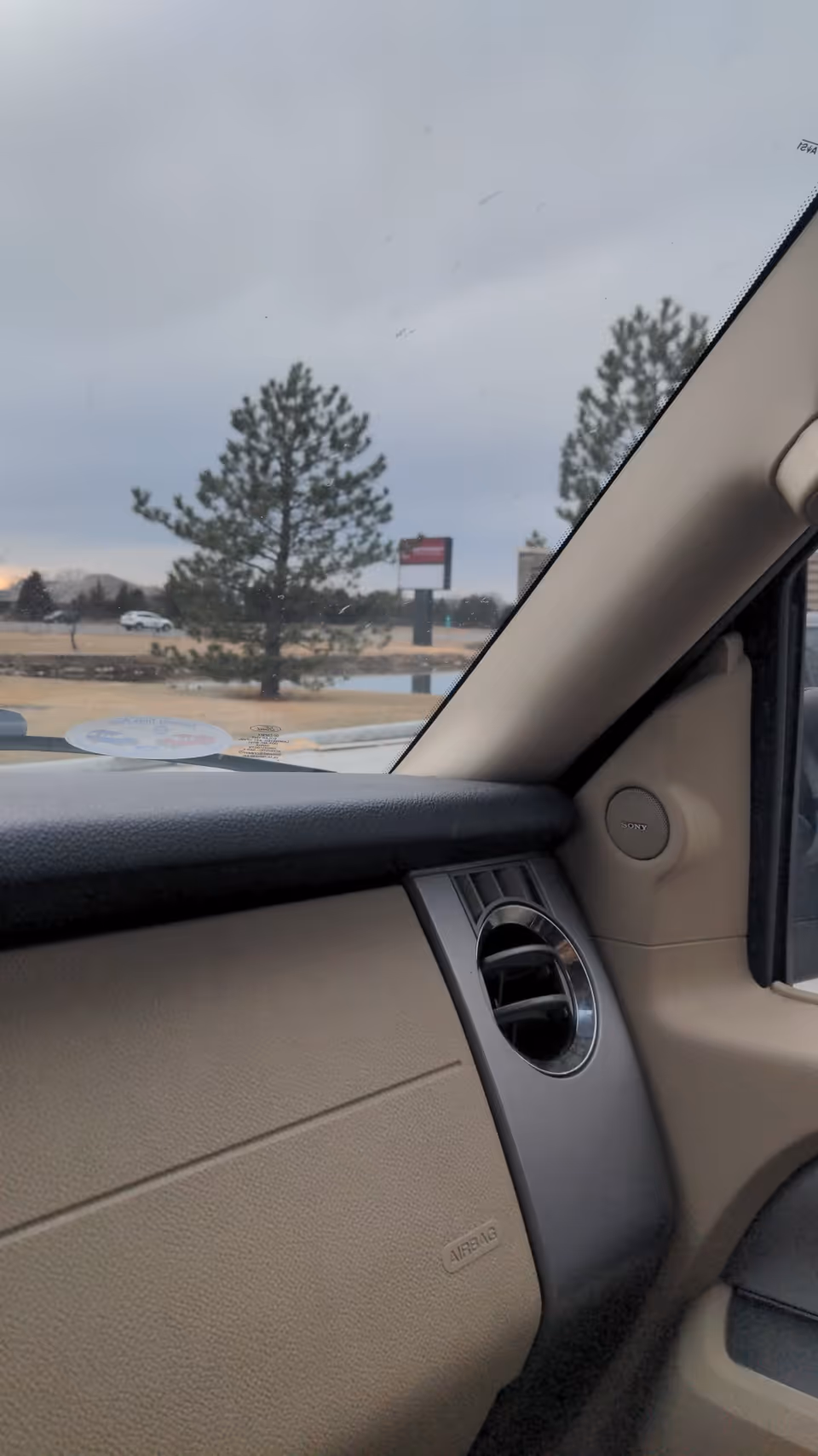 Beige car interior with dashboard and outside trees visible through window.