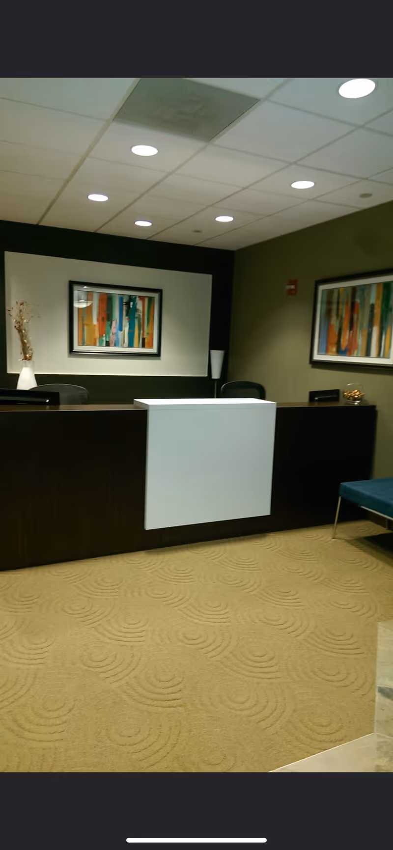 Lobby reception desk in a softly lit space with abstract art and beige carpet.