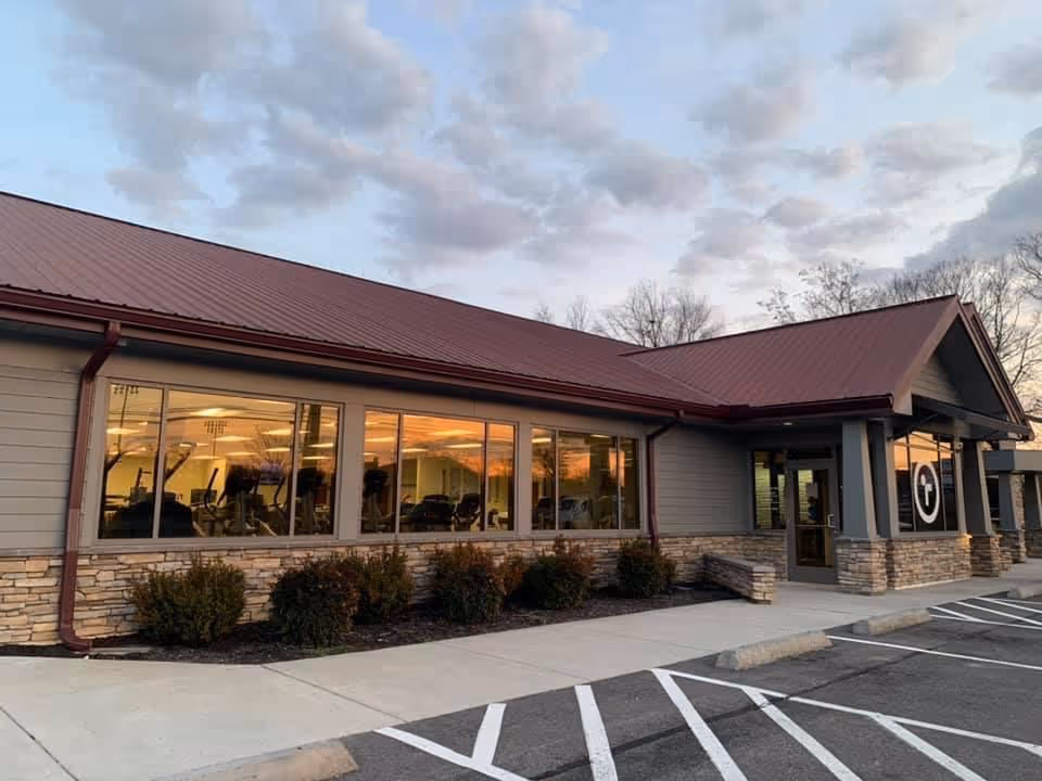 Exterior view of a single-story facility with large windows showing an indoor exercise area.