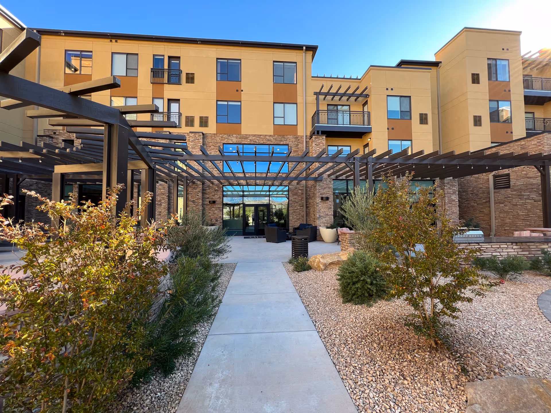 Modern senior living building exterior with a courtyard and outdoor seating under a pergola.