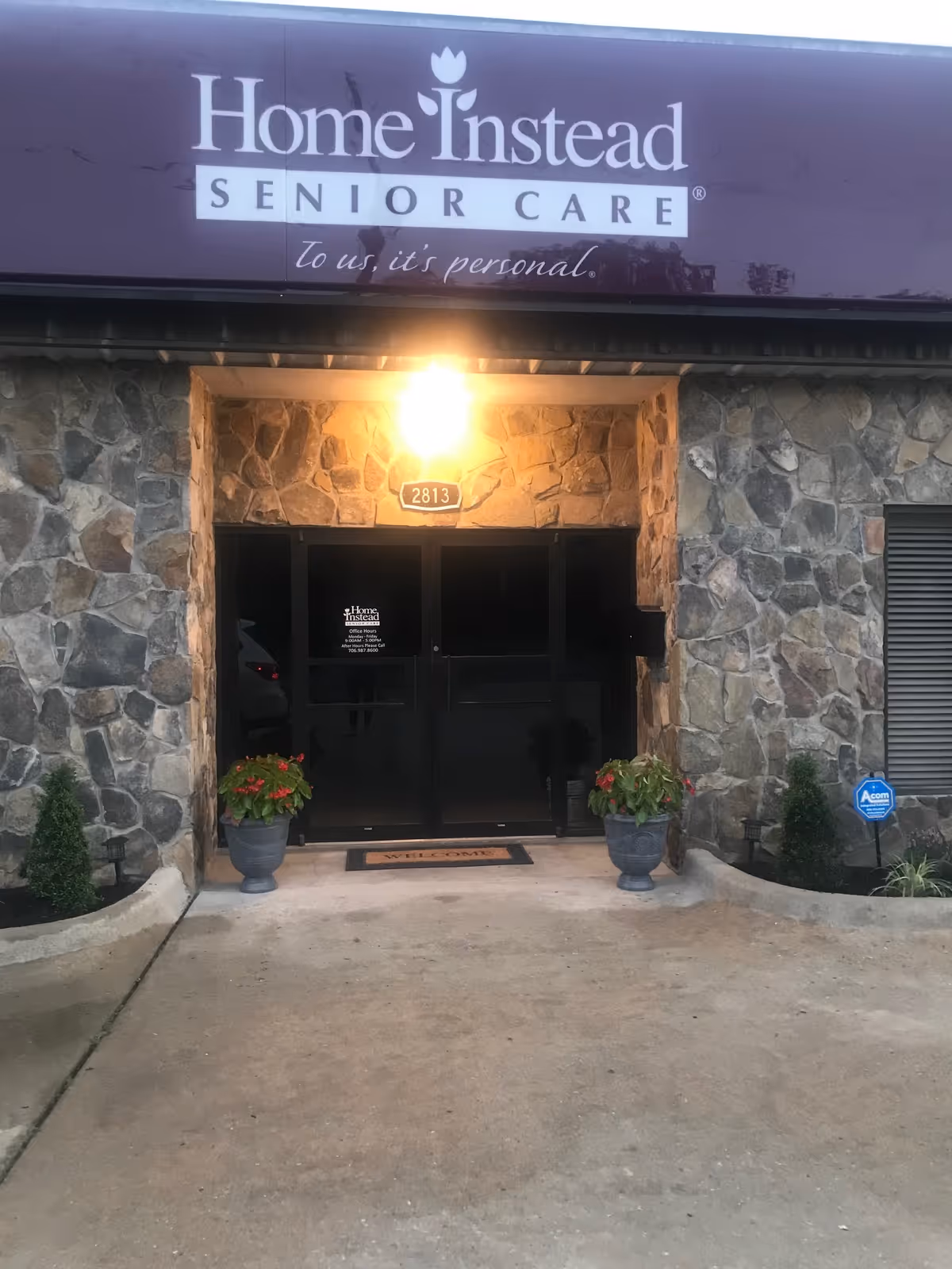 Stone exterior entrance of Home Instead Senior Care with potted plants and a welcome mat