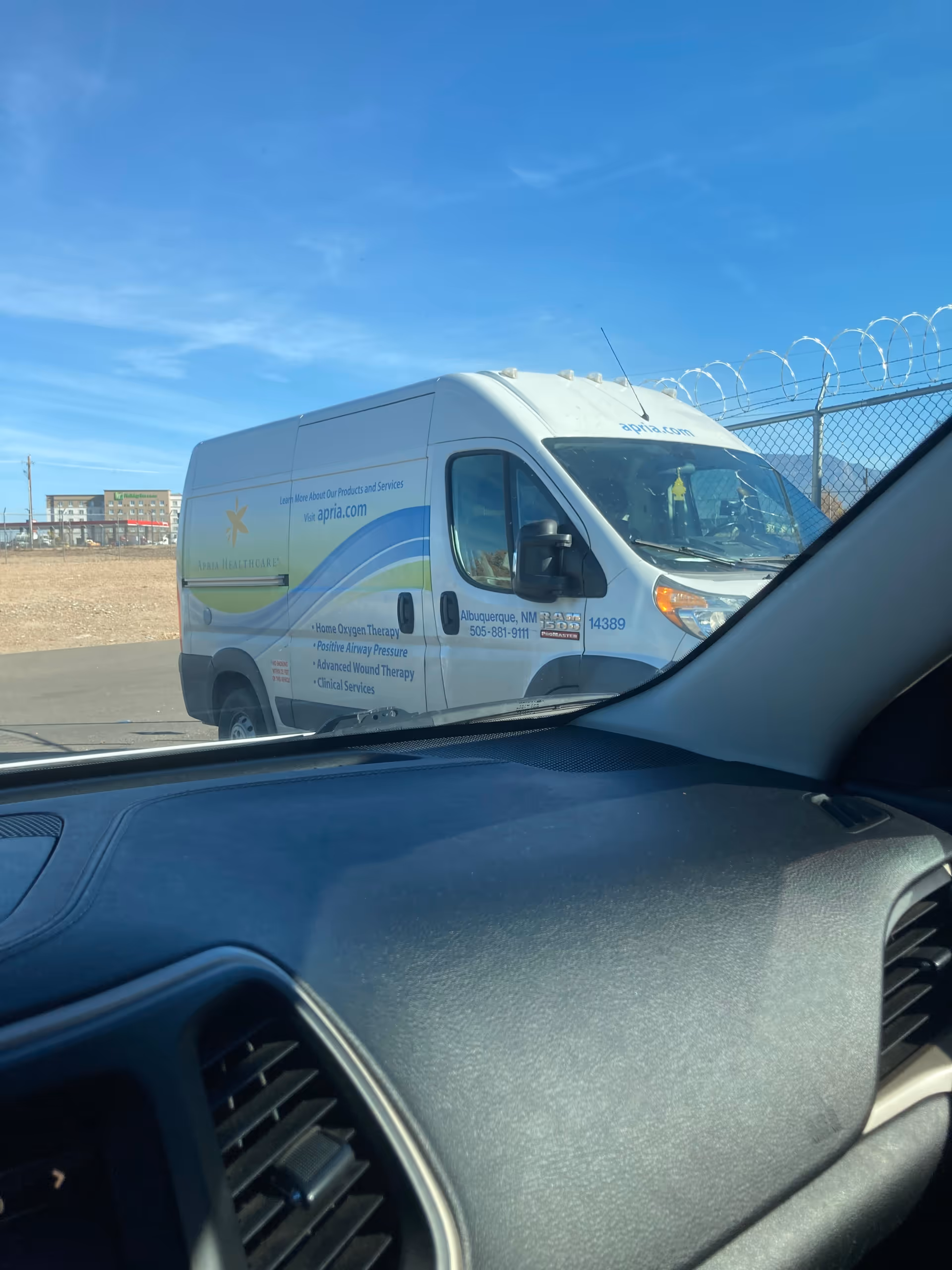 White Apria Healthcare van parked outside beside a barbed-wire fence.