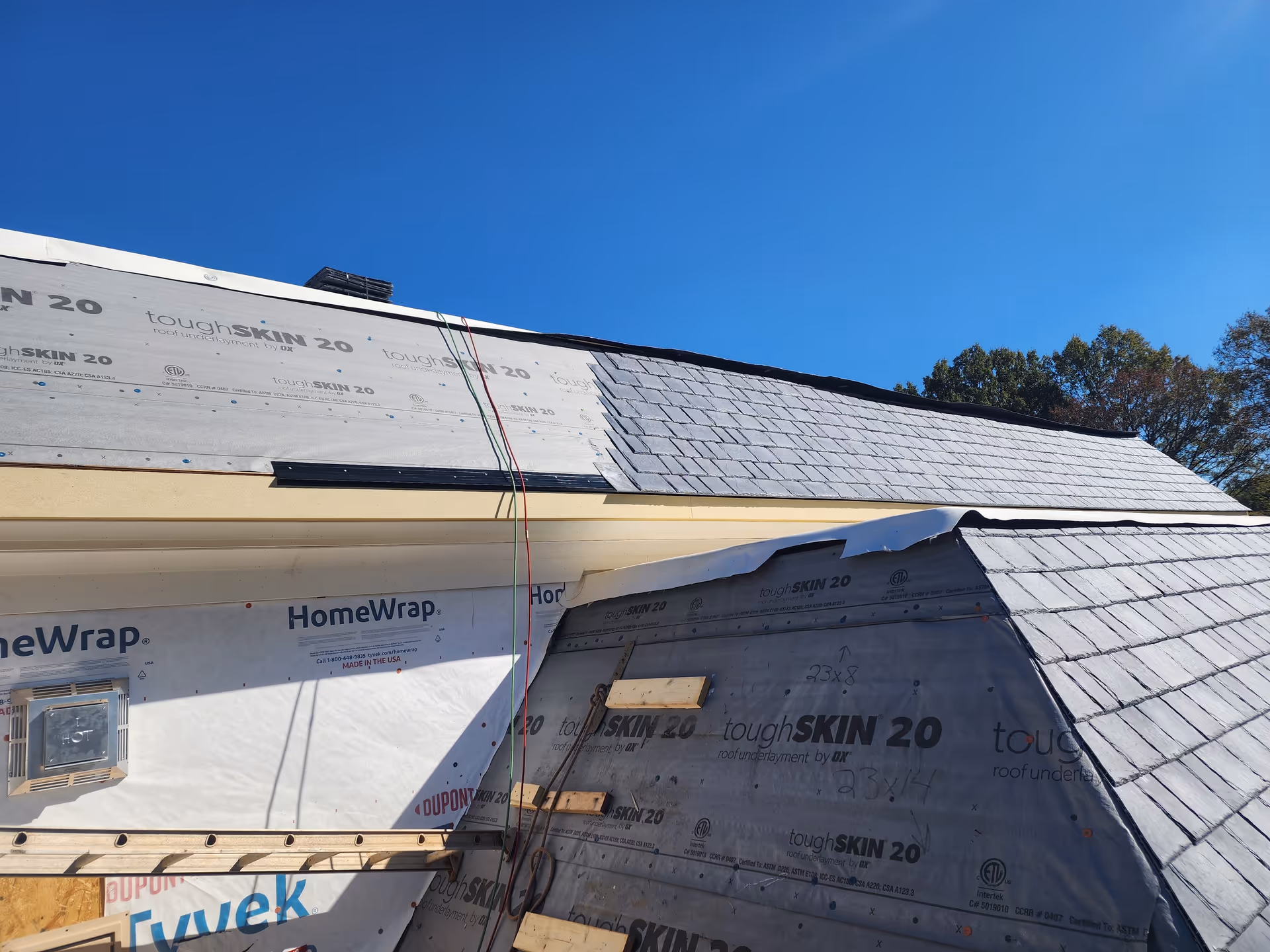 Roof of a building under construction with exposed underlayment and shingles.