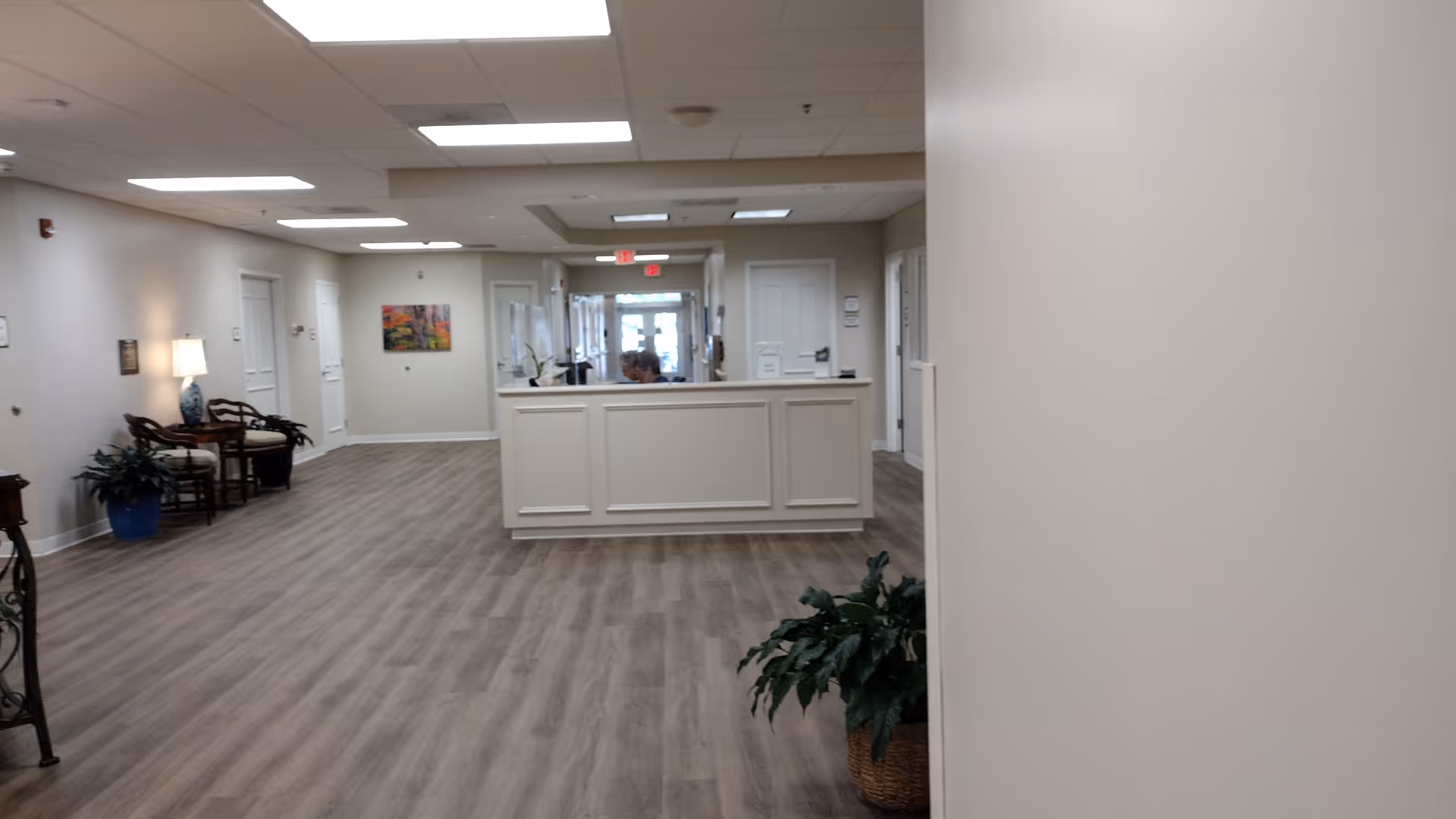 Bright lobby/reception area with central front desk and hallways in a neutral senior care facility.