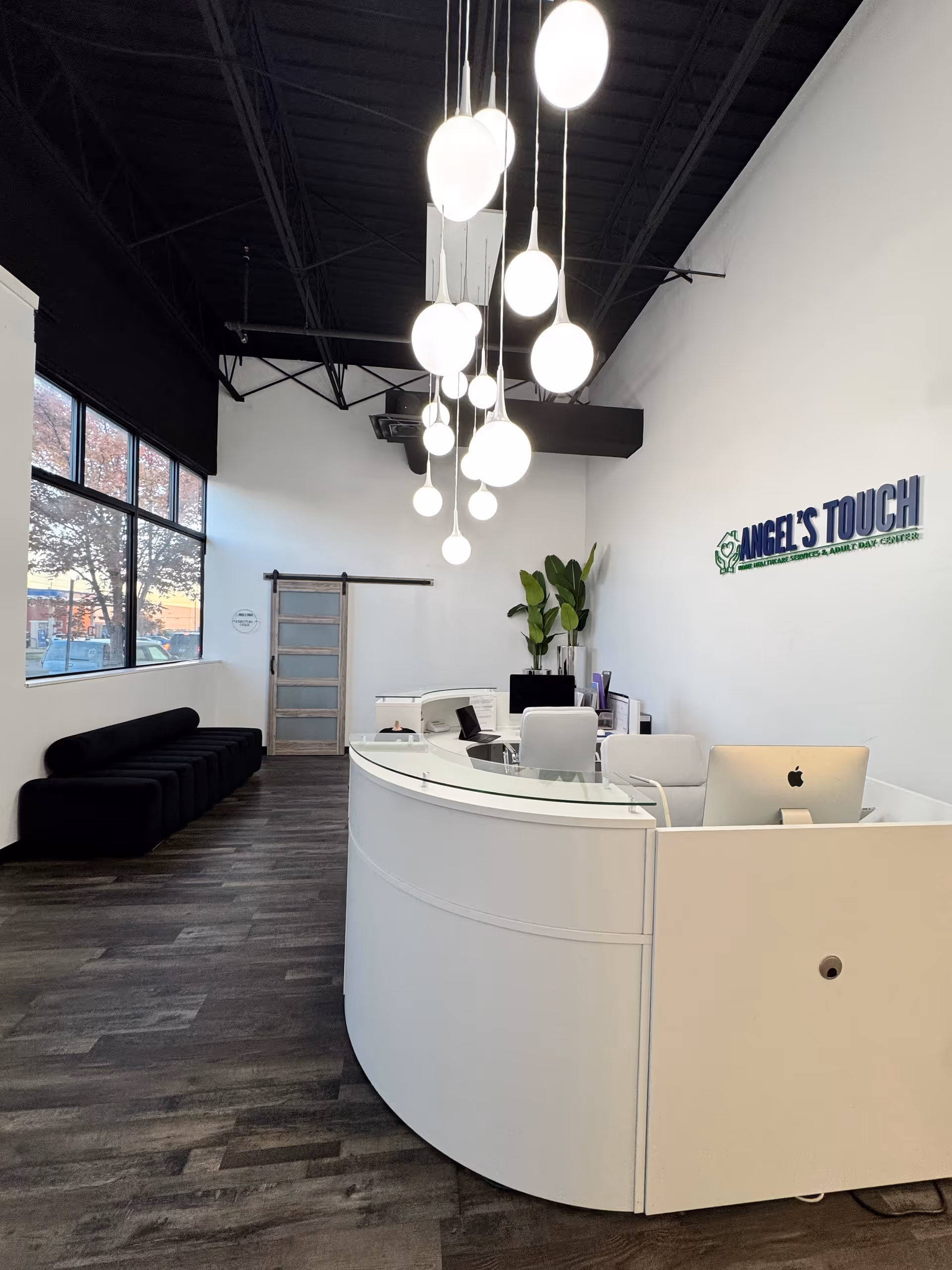 Modern reception area with curved white desk, hanging pendant lights, and Angel's Touch logo wall.