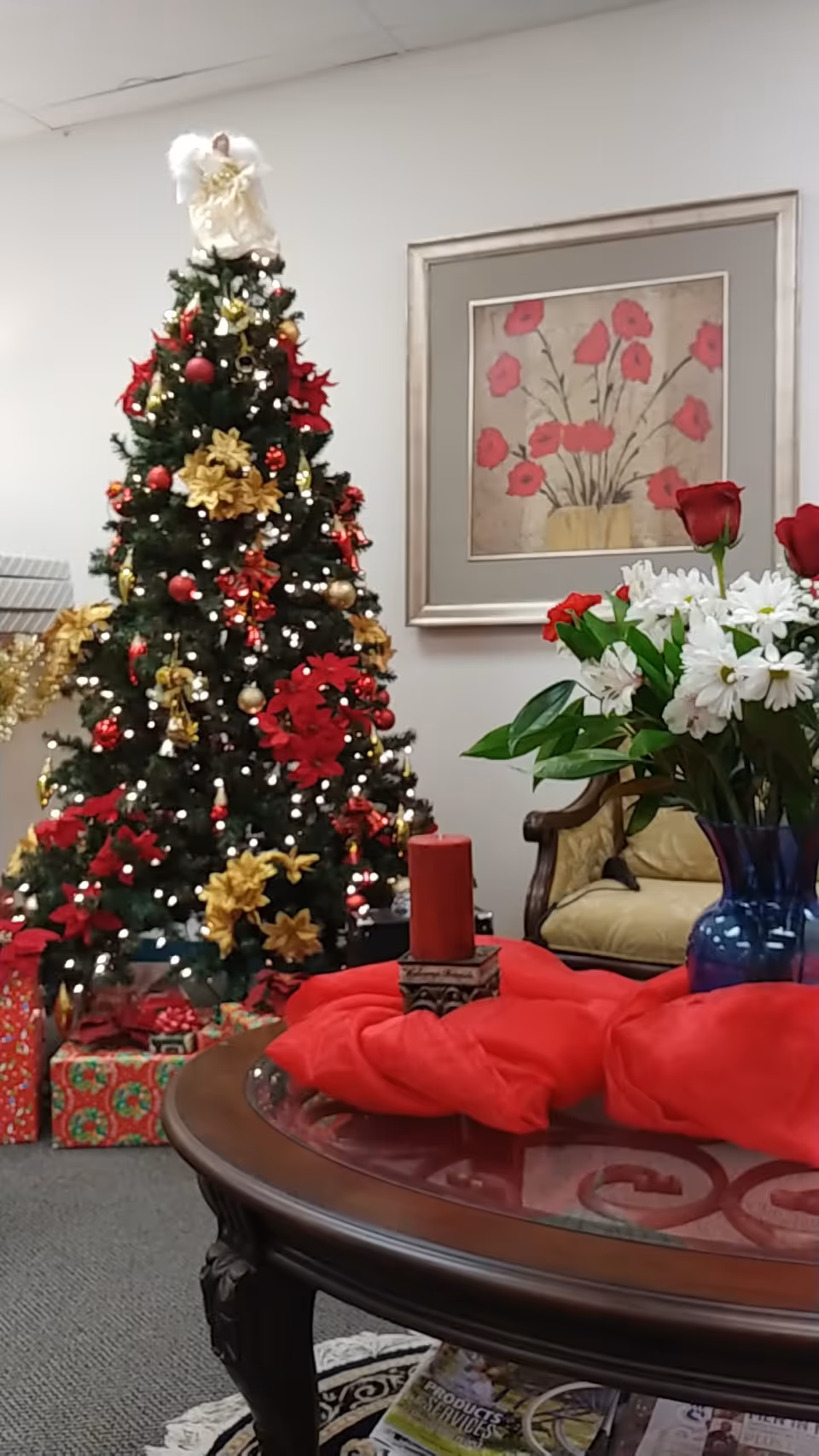 A decorated Christmas tree with gifts and flowers in a cozy lobby.
