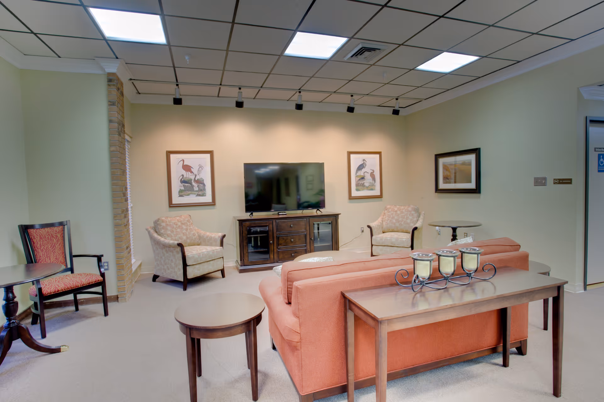 Cozy senior living lounge with coral sofa, armchairs, coffee tables, and a TV.