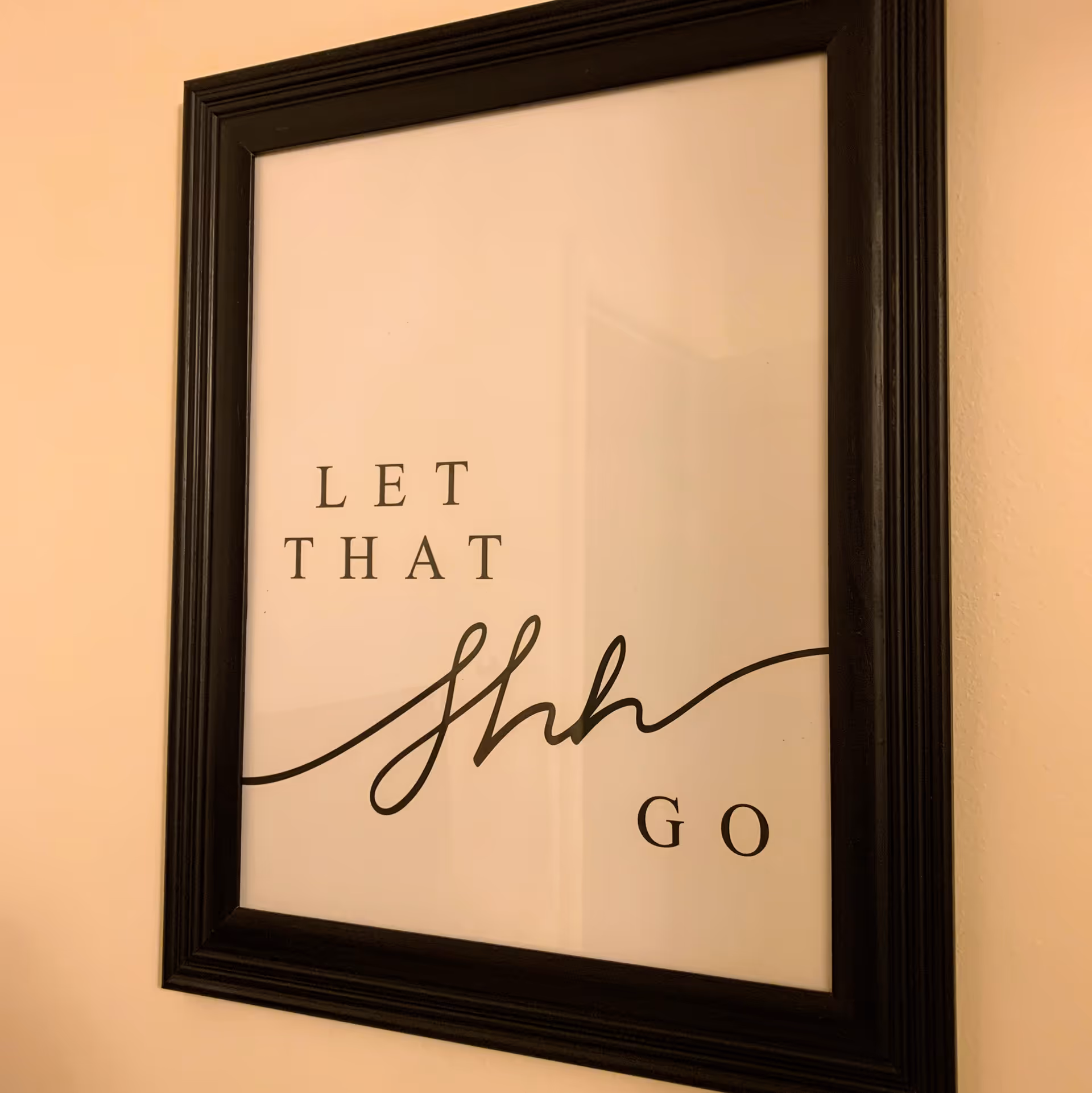 Framed wall art shows the phrase 'LET THAT SHH GO' on a beige wall.