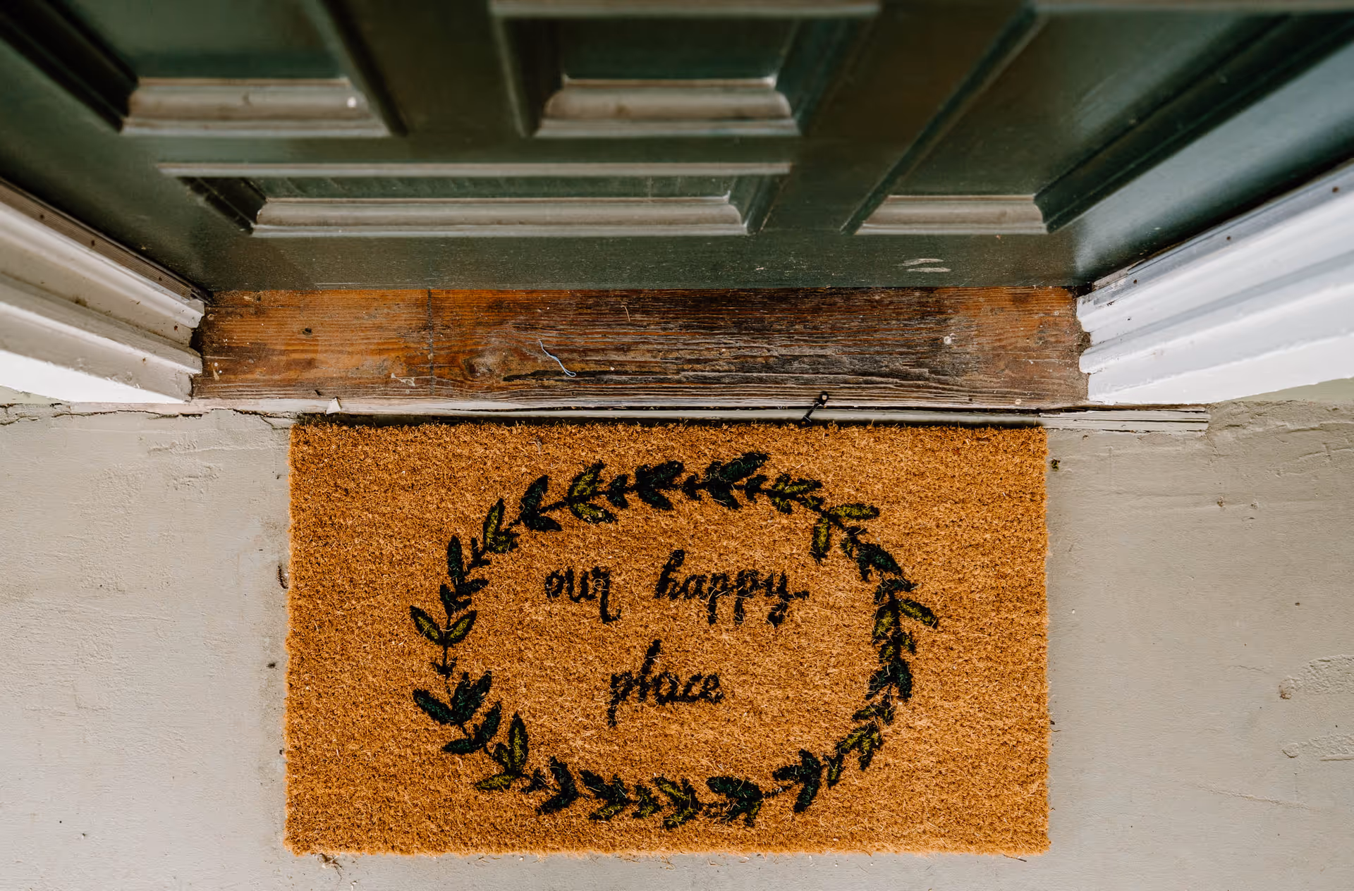 Close-up of a door threshold with a doormat reading 'my happy place'.