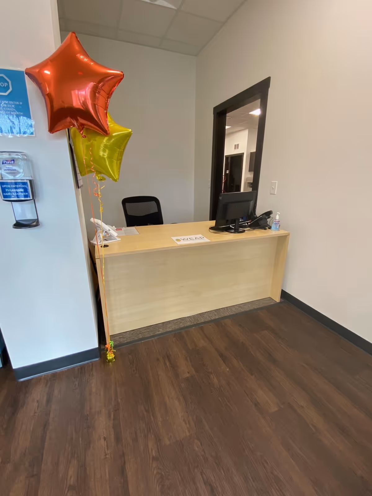Reception desk with computer, balloons, and hand sanitizer in a facility lobby.