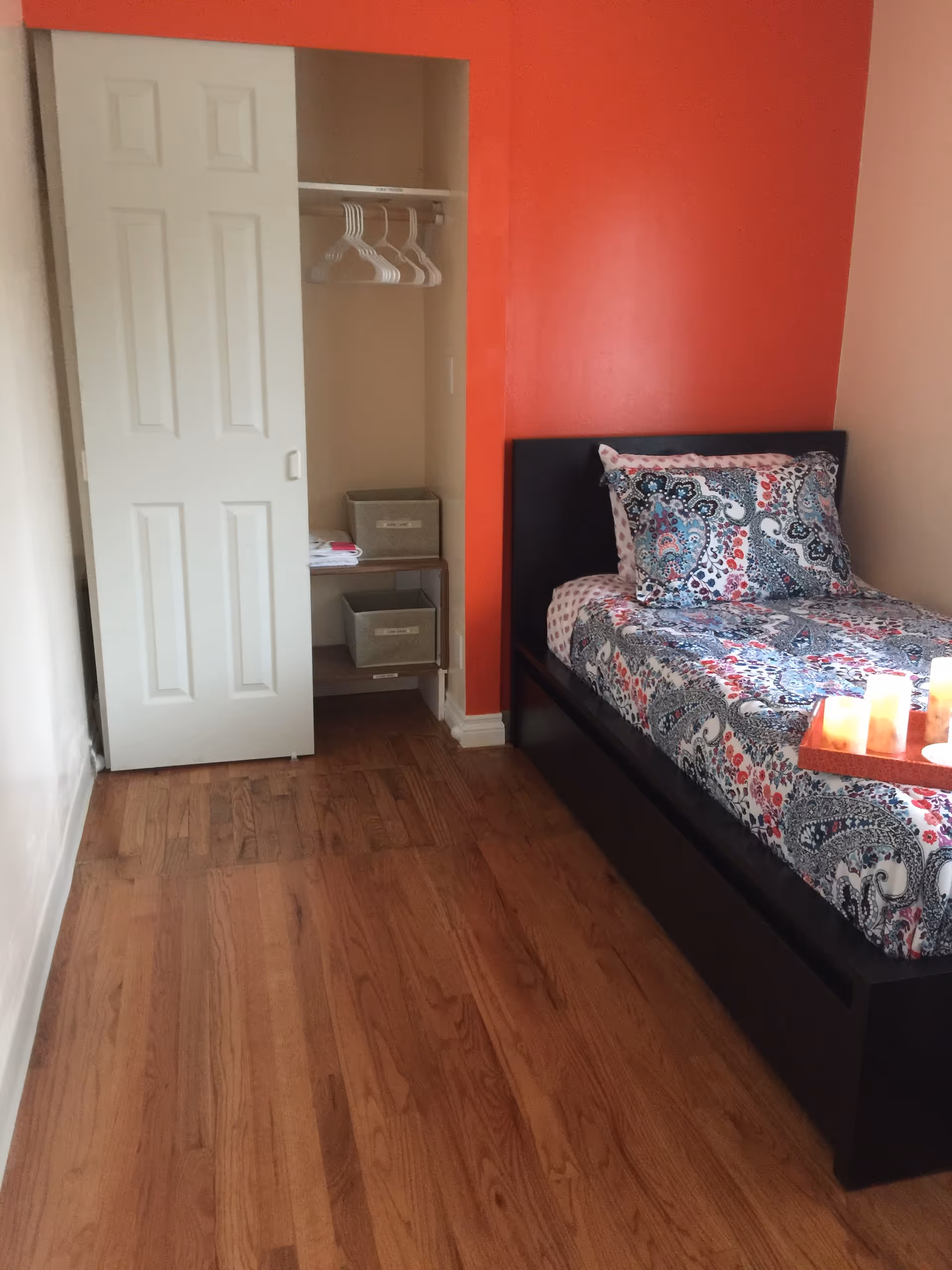 Bedroom with a bed, open closet, and an orange accent wall.