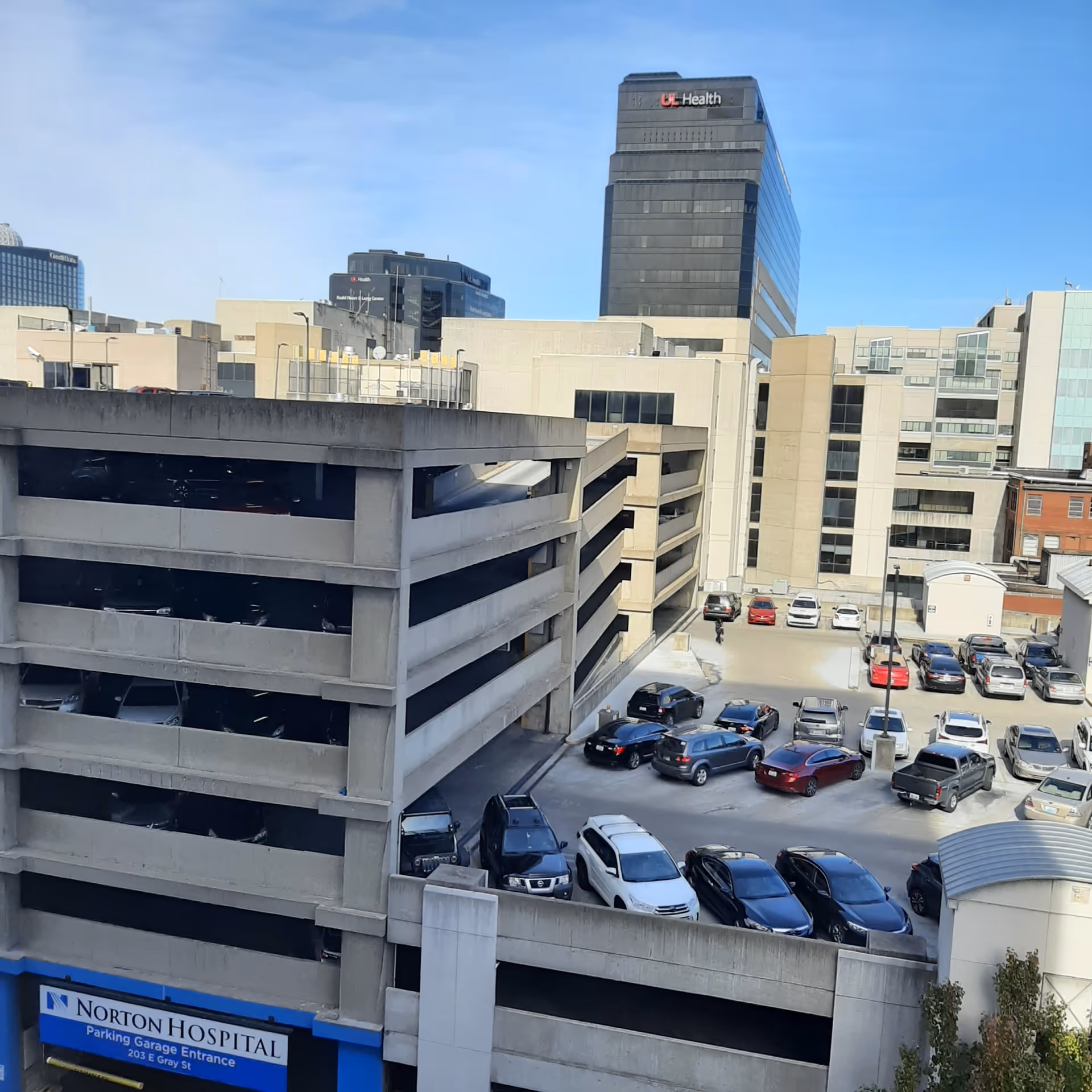 Urban hospital campus with a multi-level parking garage and surrounding beige office buildings.