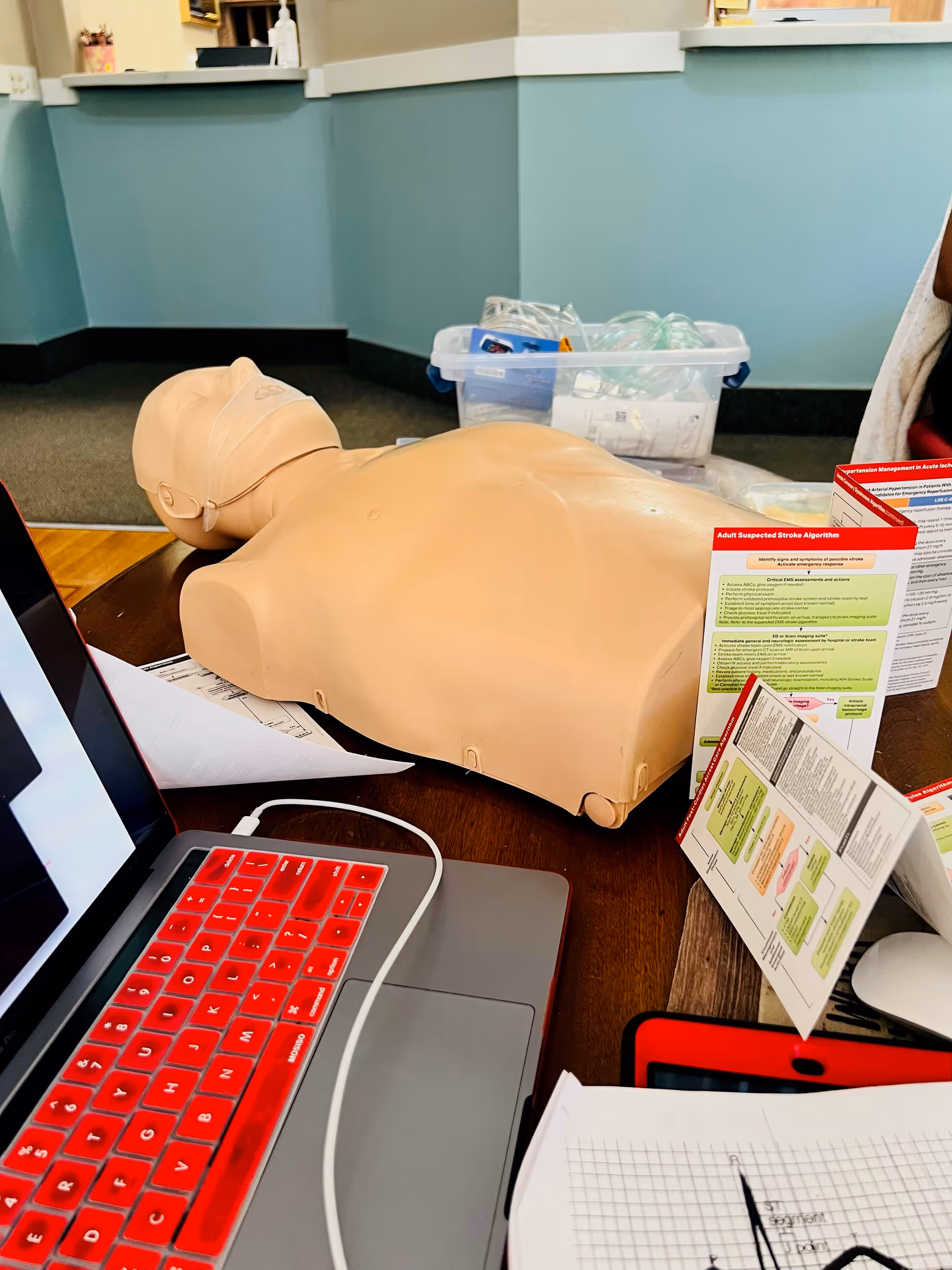CPR training mannequin on a desk with a laptop and brochures.