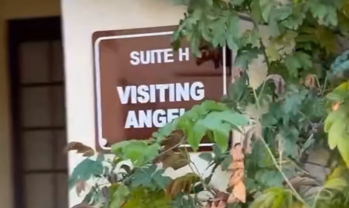 Sign reading Visiting Angels on exterior wall, partially obscured by foliage.