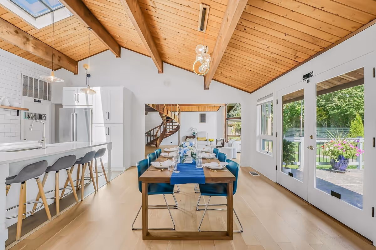Bright open dining area with a wooden ceiling, kitchen island, and blue chairs.