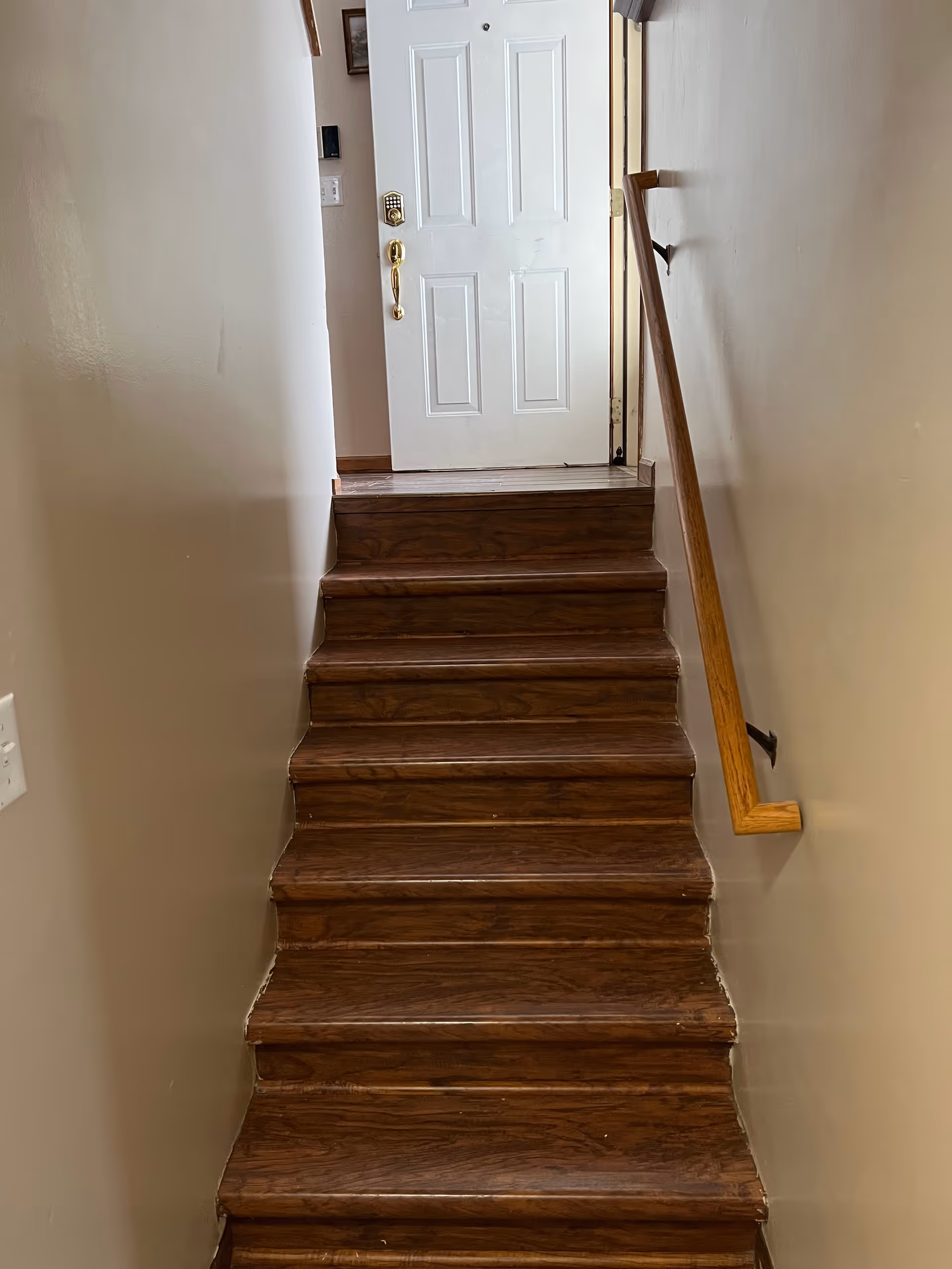 Narrow wooden stairs with a handrail lead up to a closed white door.