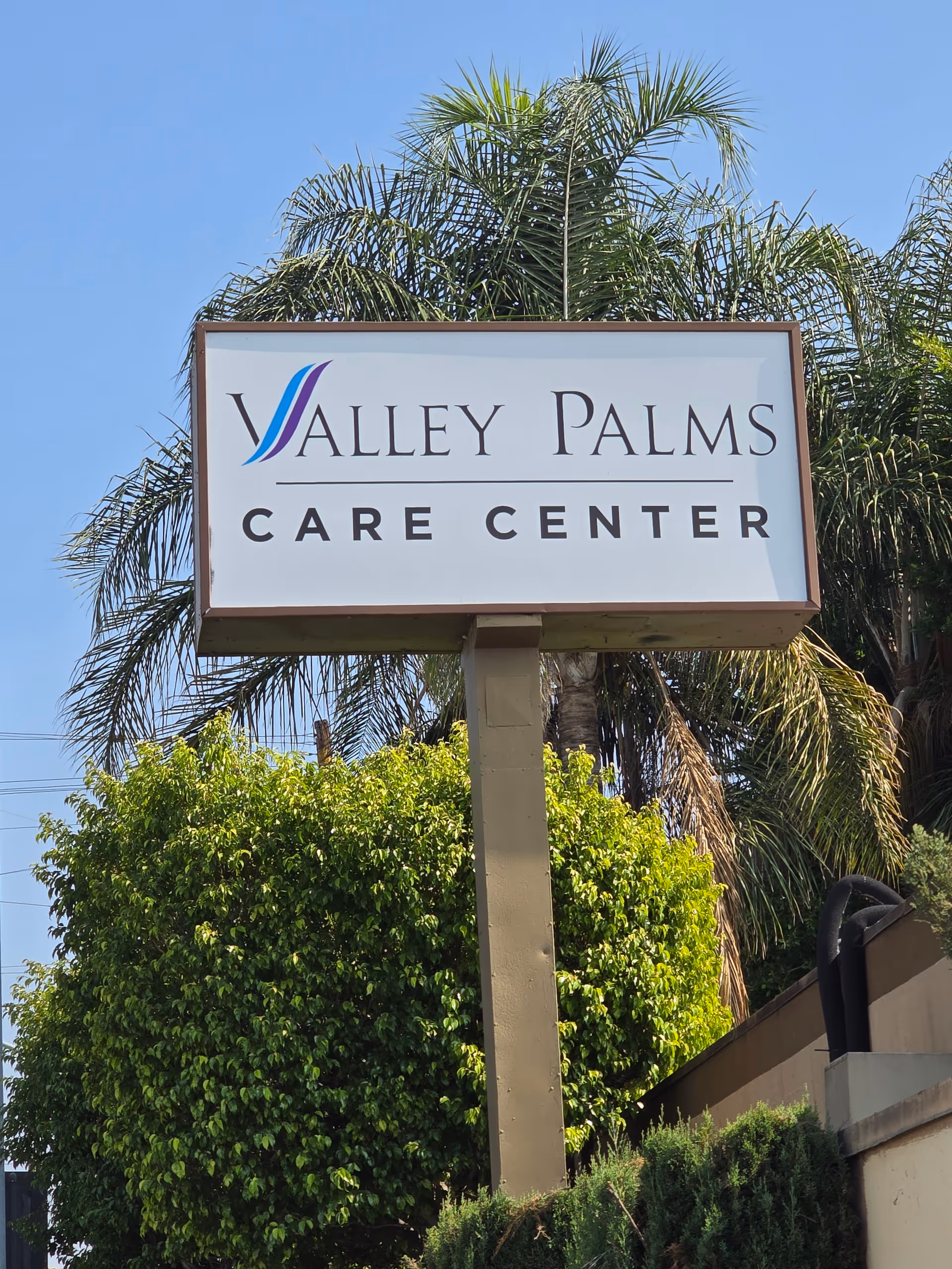 Outdoor sign for Valley Palms Care Center with palm trees and greenery.