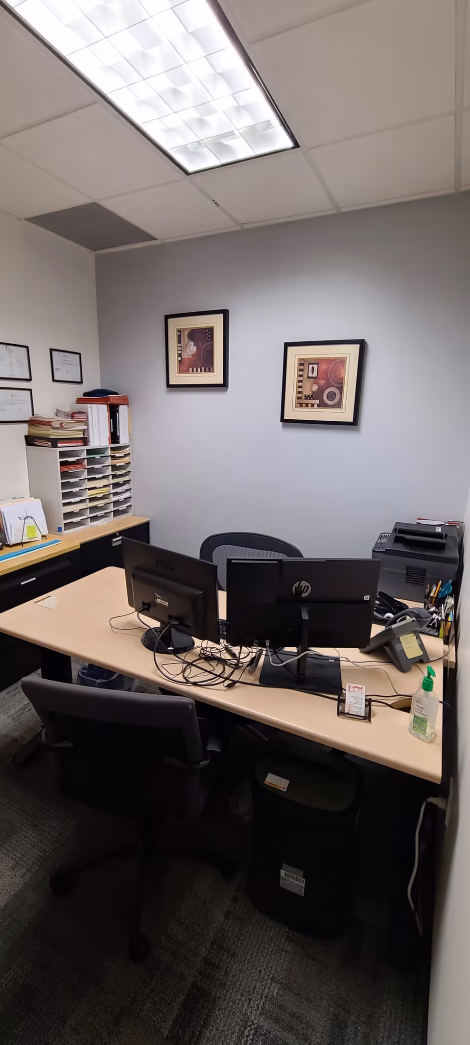 Small office with two computer monitors, printer, and organized filing shelves.
