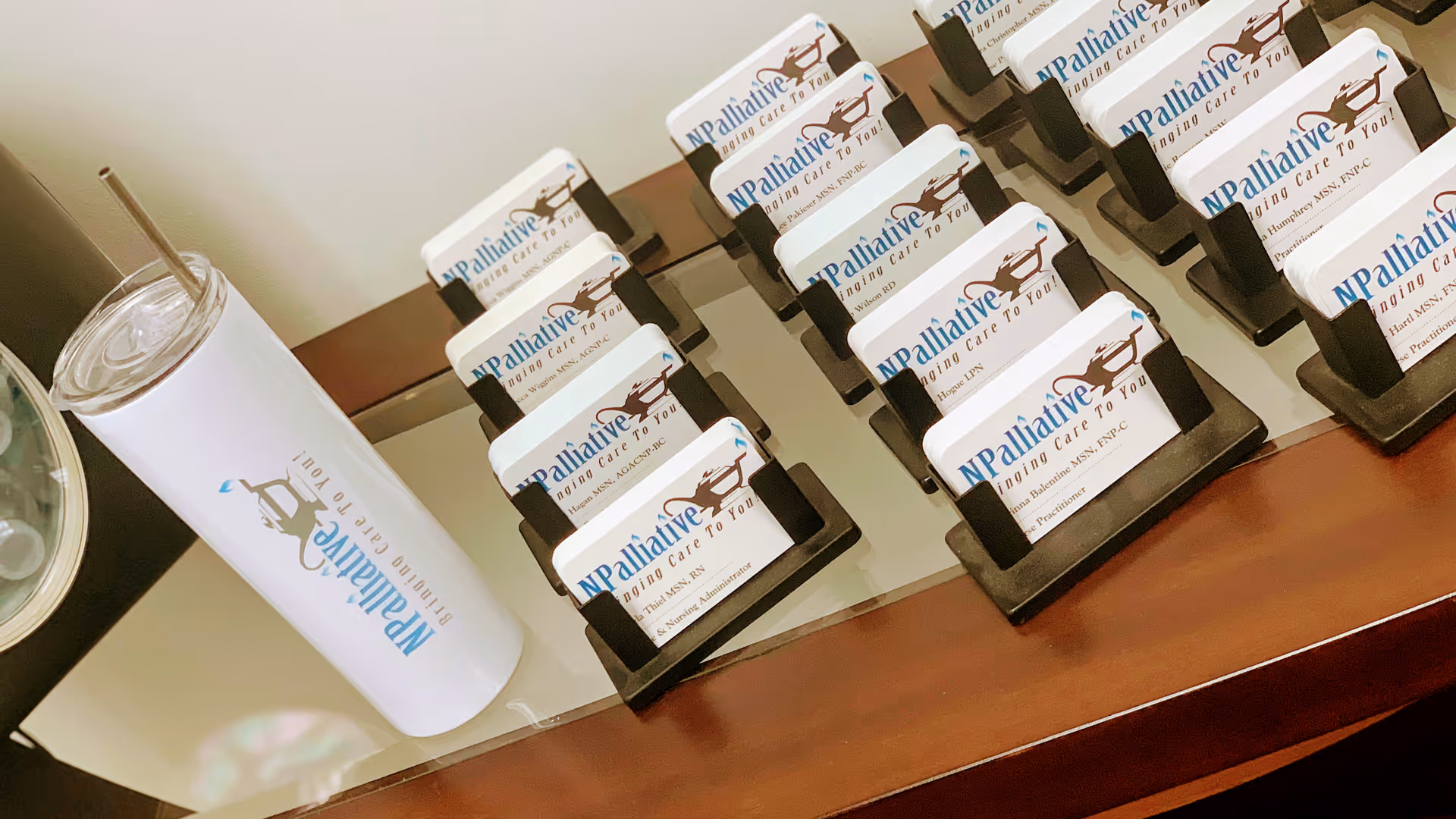 Close-up of multiple NPalliative-branded name tags on a desk beside a white tumbler.