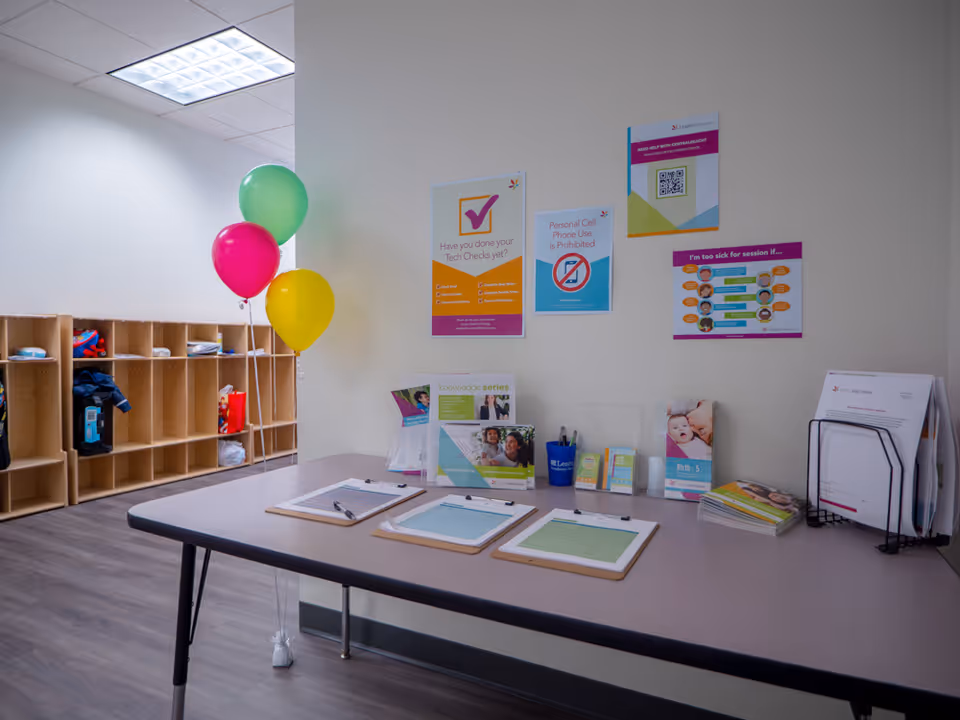 Interior reception area with a table, posters, brochures, and colorful balloons along the wall.