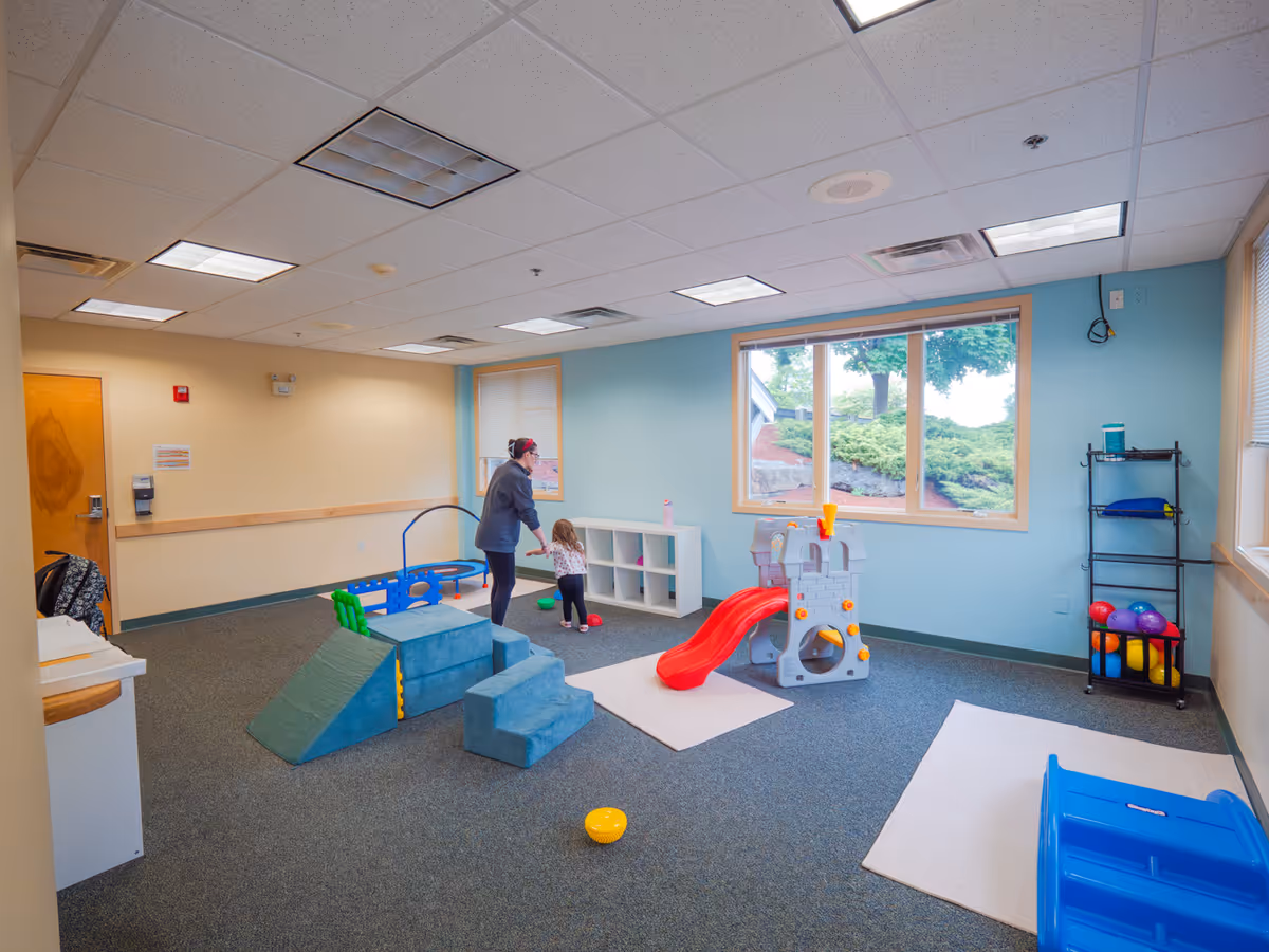 Indoor playroom in a senior facility with foam blocks and a caregiver with a child.