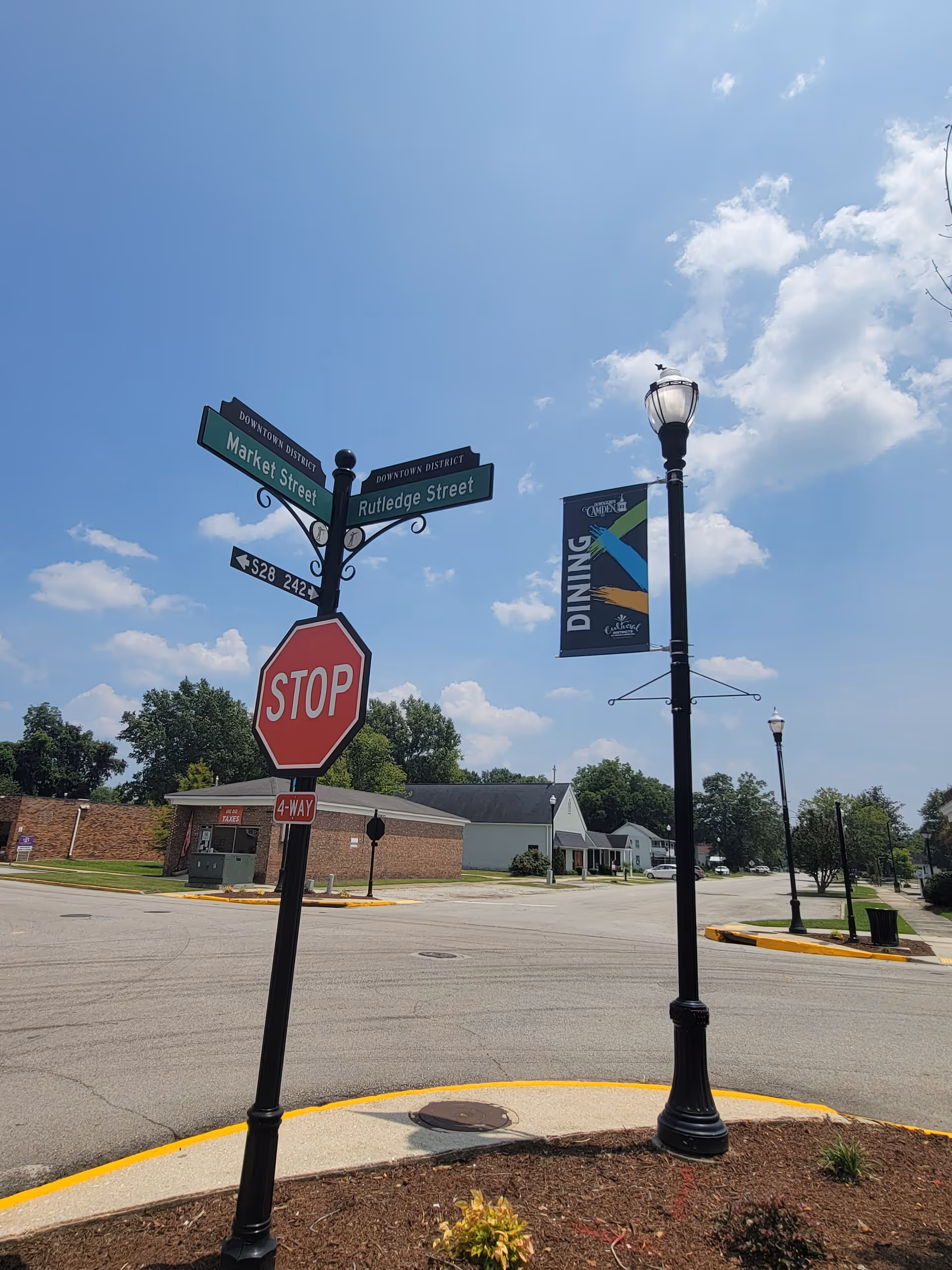Street intersection with stop sign, street signs, lamp posts, and a distant building under blue sky.