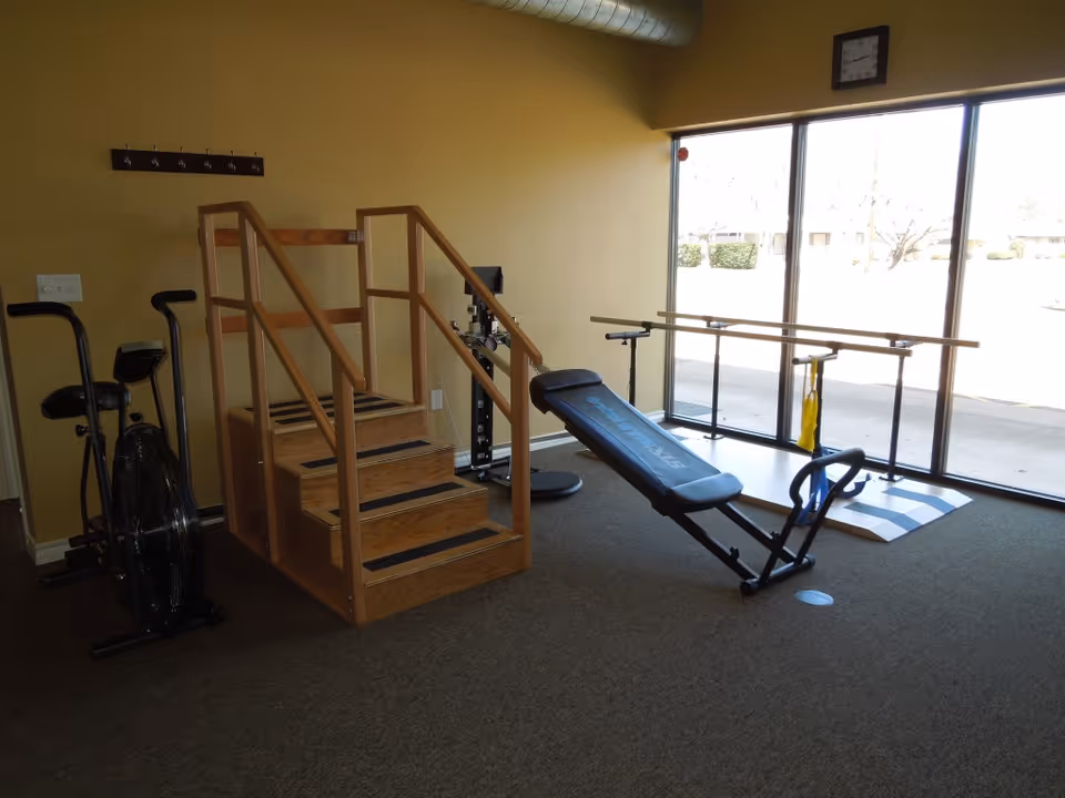 Interior fitness room with a stationary bike, wooden stairs, incline bench, and parallel bars.