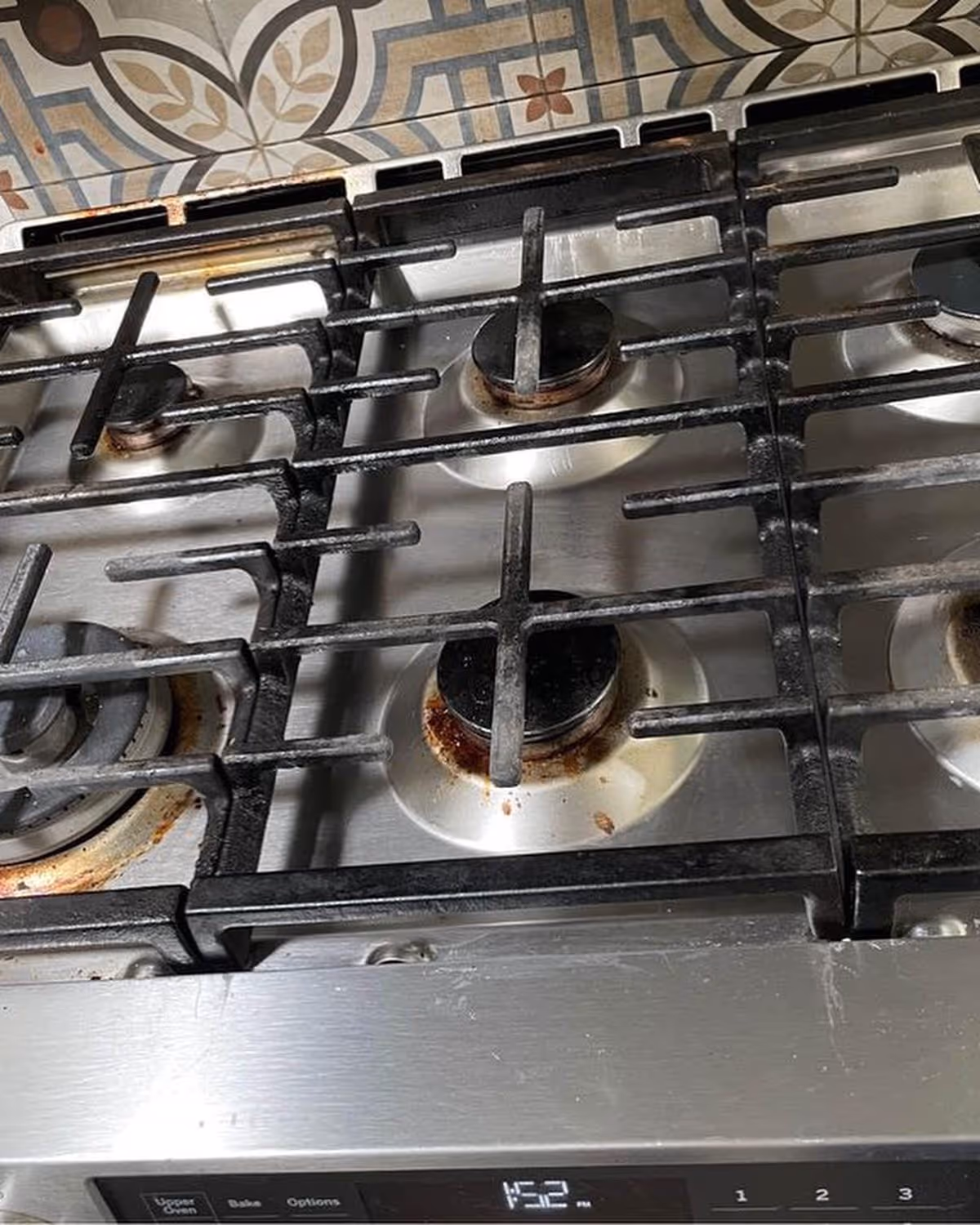 Close-up of a stainless steel gas stove with rust around burners in a kitchen.