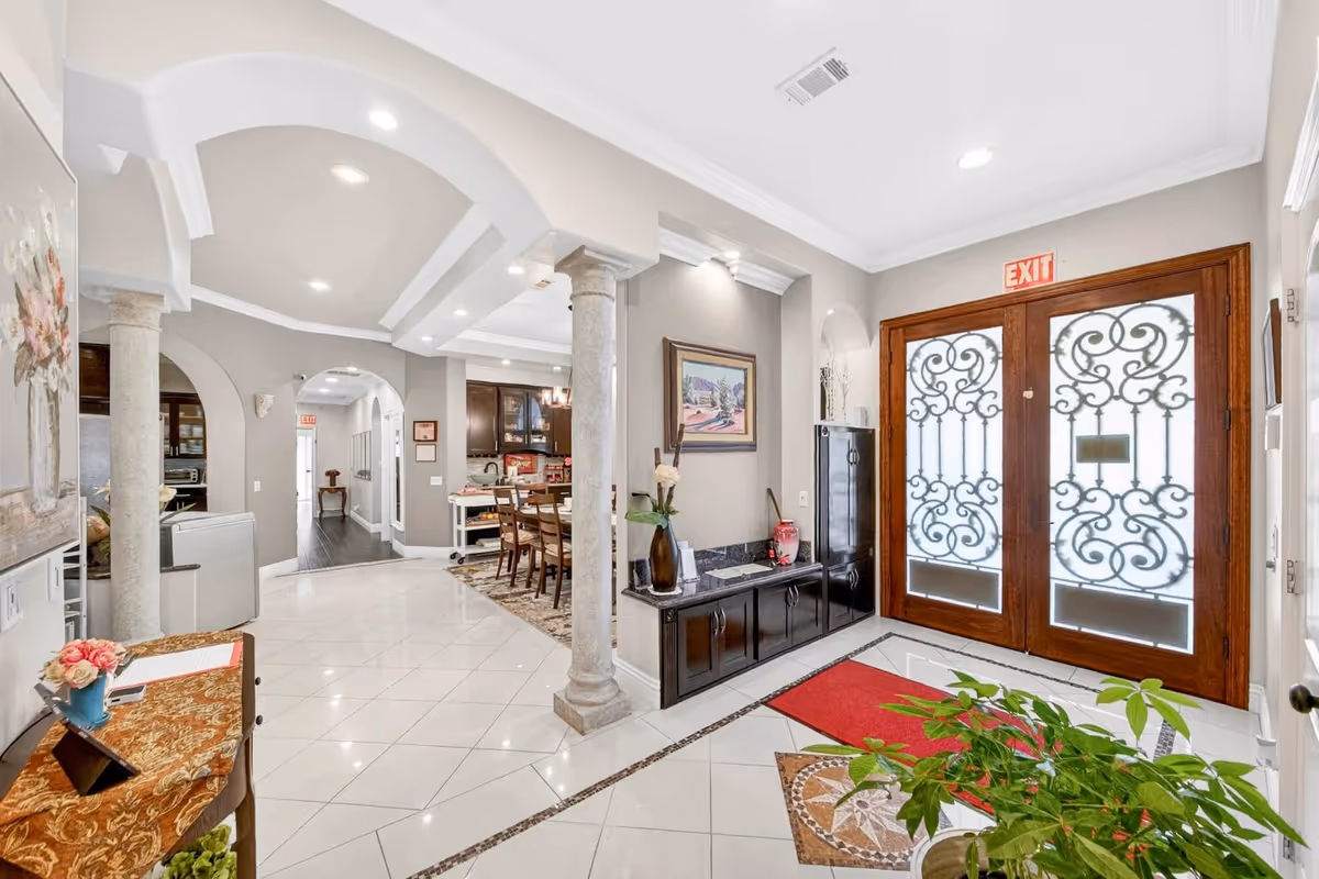 Bright lobby with ornate double doors, columns, and seating area in a senior living facility.