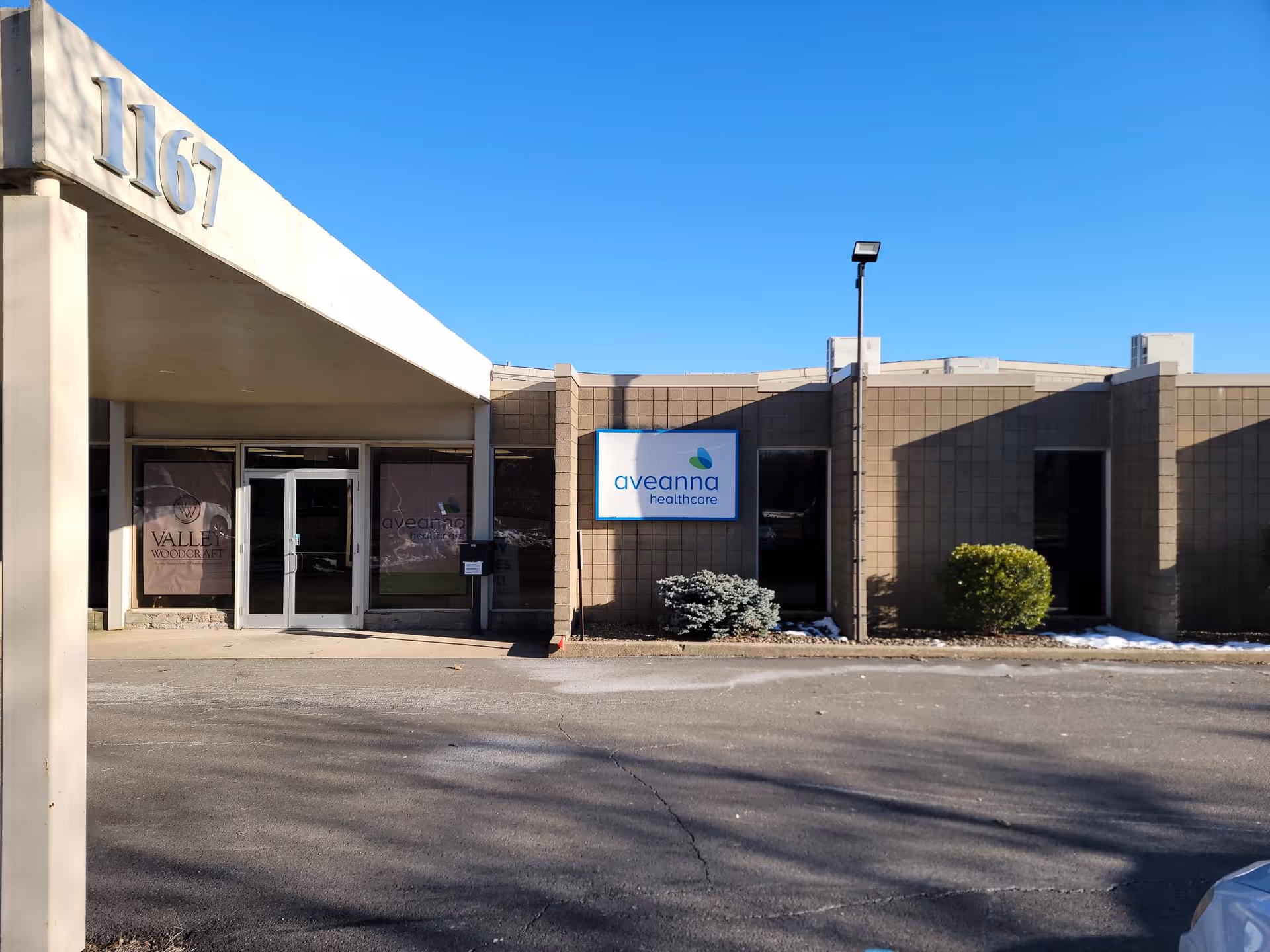 Front exterior of Aveanna Healthcare facility with entrance doors and sign beneath a clear blue sky.
