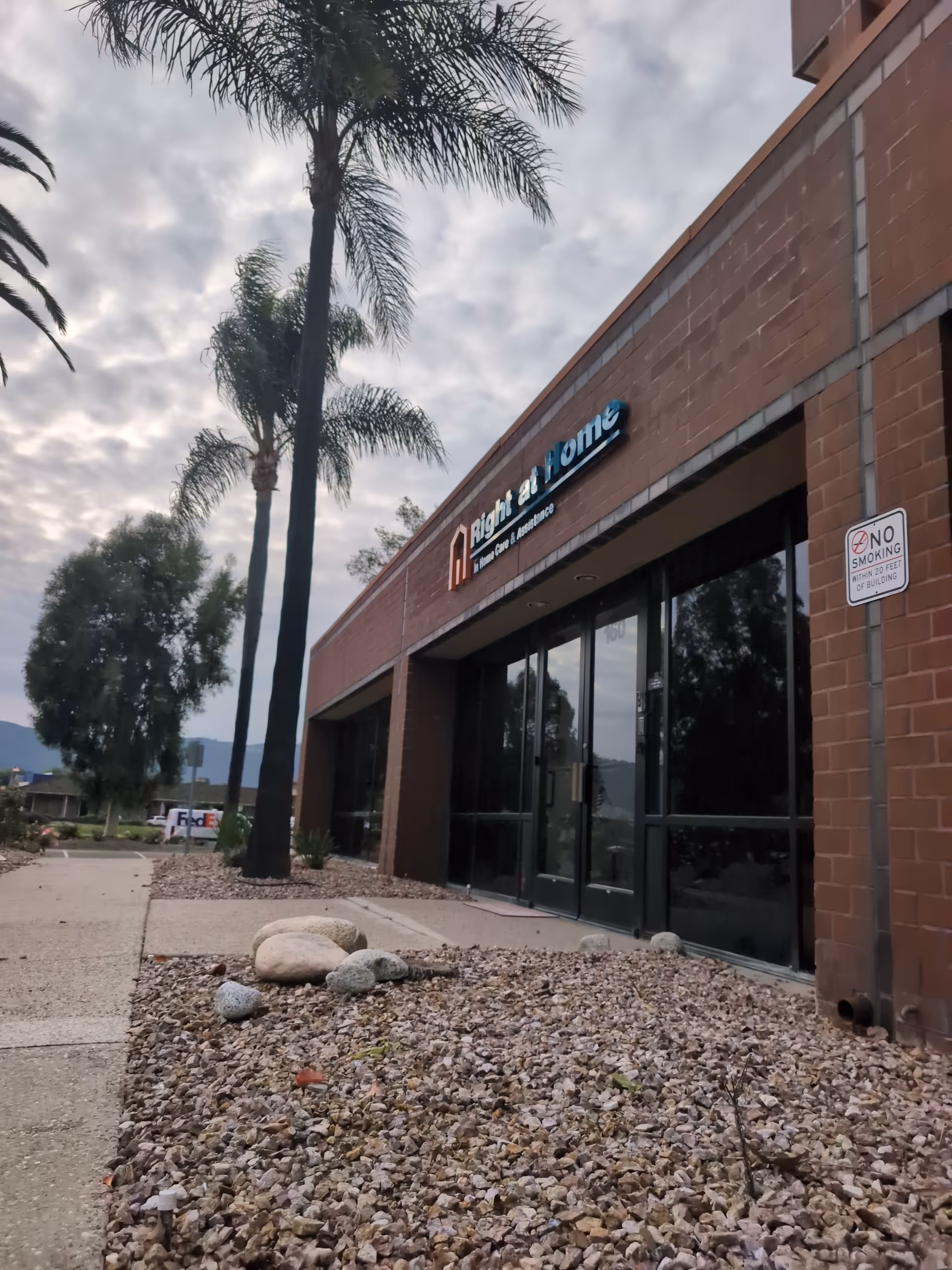 Exterior view of a Right at Home facility with palm trees and rocky landscaping.