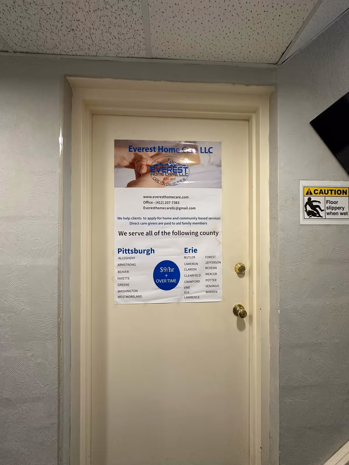 White door with Everest Home Care LLC poster, caution sign, and textured hallway walls.
