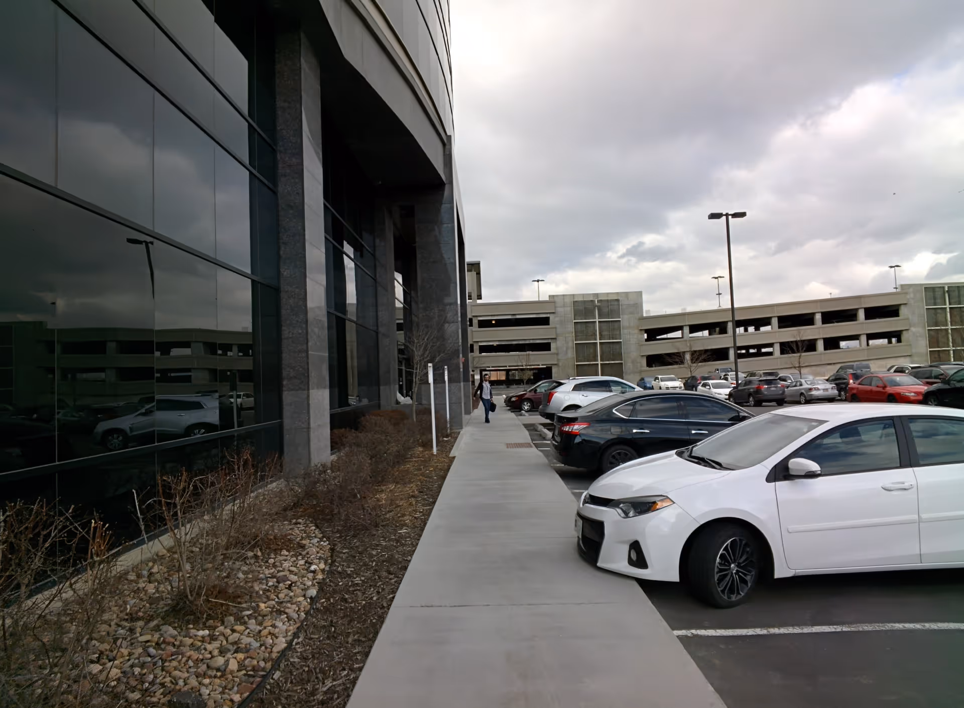 Exterior view of a modern building with glass facade, sidewalk, and parking lot.