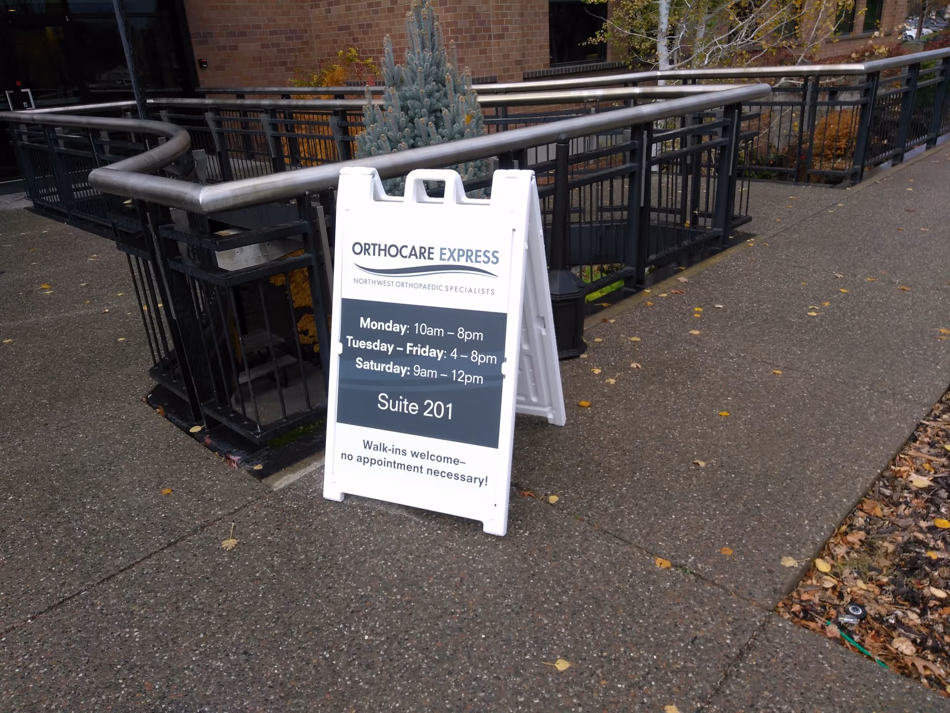 White A-frame sign on a sidewalk outside a brick building.