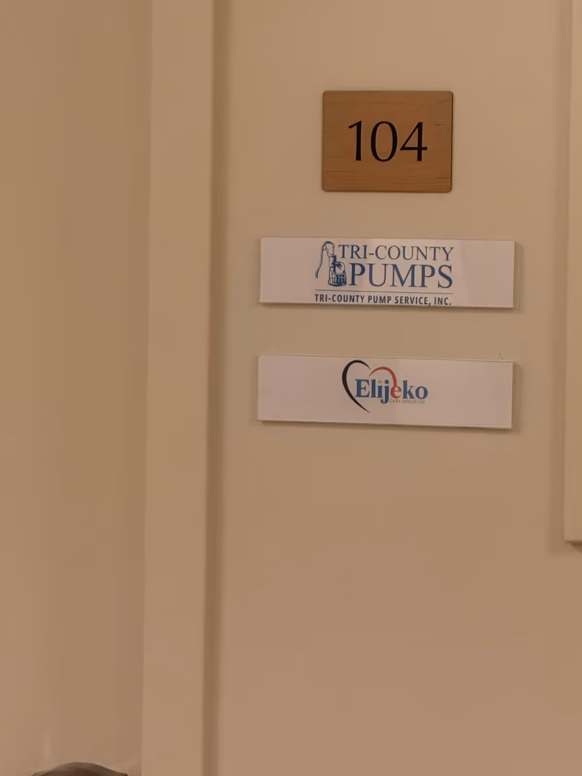 Hallway wall showing room 104 sign and two facility company plaques.