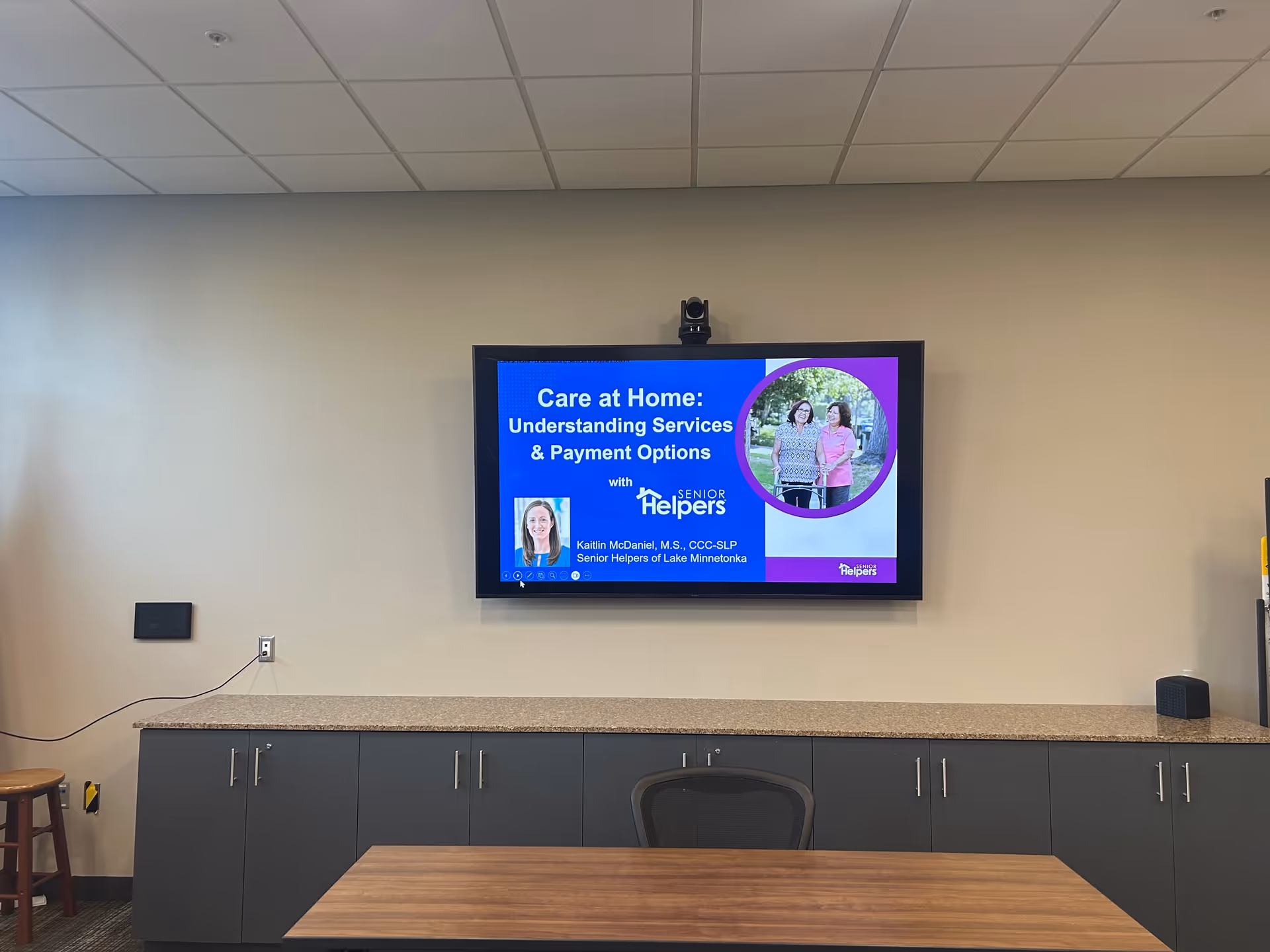 A conference room with a wall-mounted screen displaying a Senior Helpers presentation.
