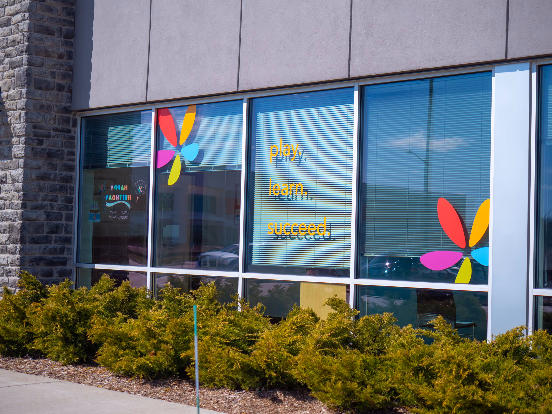Exterior view of a modern building with colorful window graphics and shrubs.