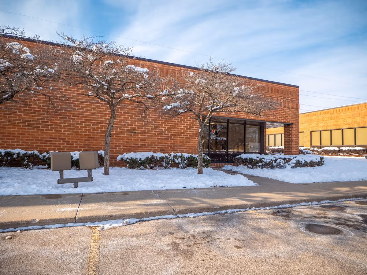 Brick building exterior with snow, leafless trees, and a glass entrance.